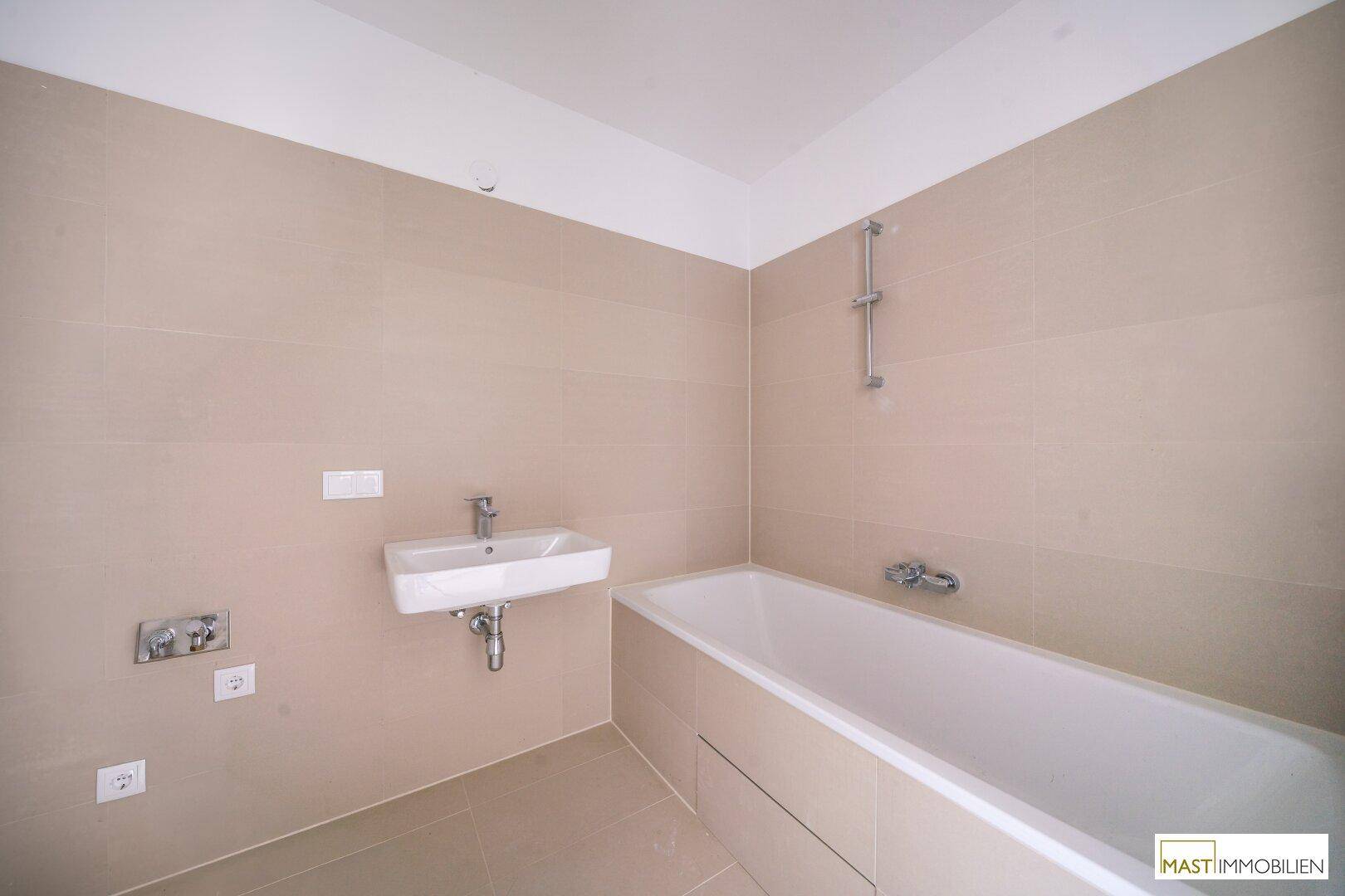 Modernes Badezimmer mit Badewanne, Waschbecken und eleganten beigefarbenen Wand- und Bodenfliesen.