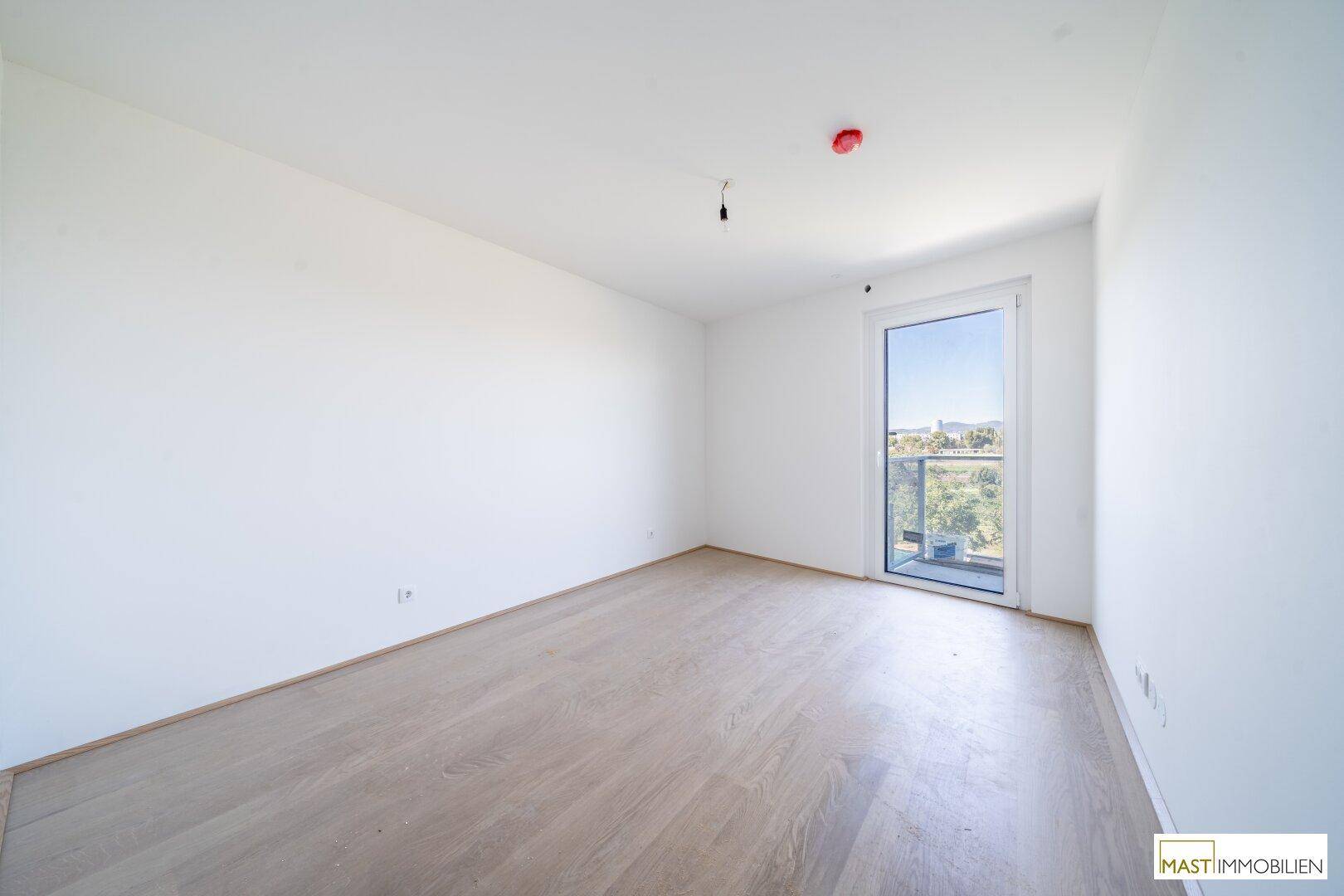 Helles Schlafzimmer mit Holzfußboden und direktem Zugang zu einem Balkon, ideal für Morgenlicht.