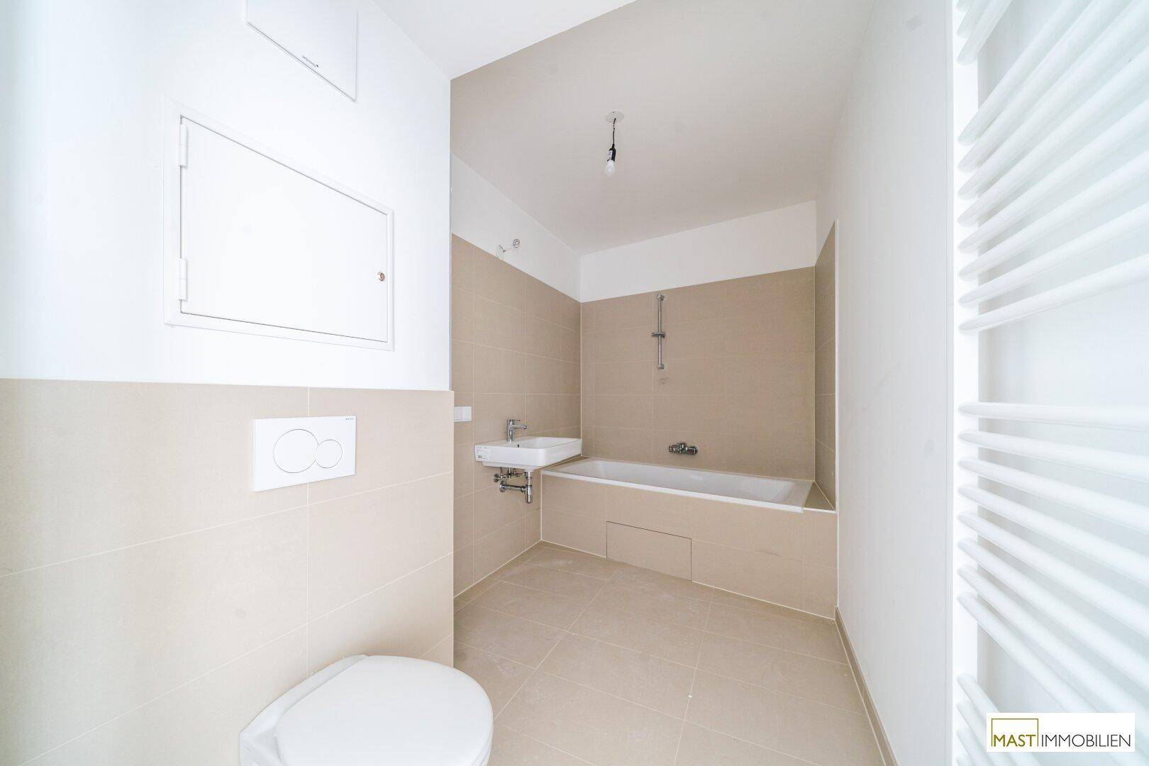 Modernes Badezimmer mit beigefarbenen Fliesen, Badewanne, WC und Handtuchheizkörper.