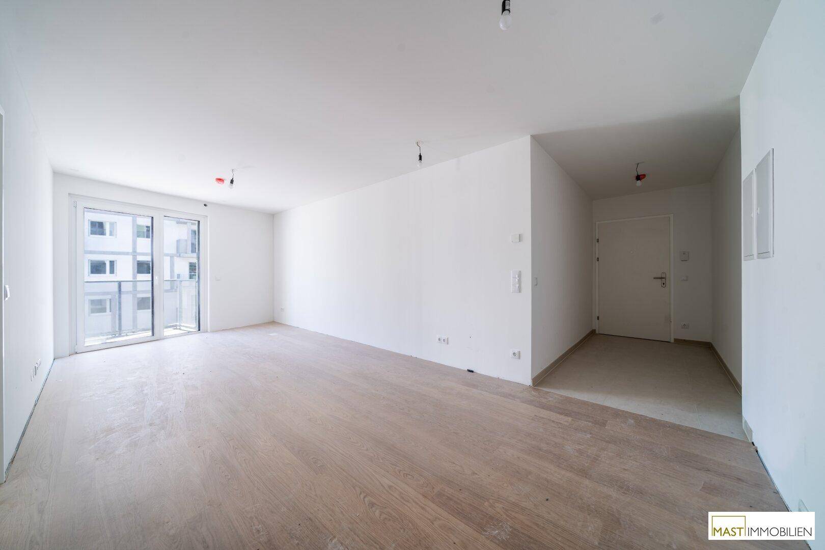Geräumiger, heller Wohnbereich mit Holzboden und Zugang zum Eingangsbereich und Balkon.