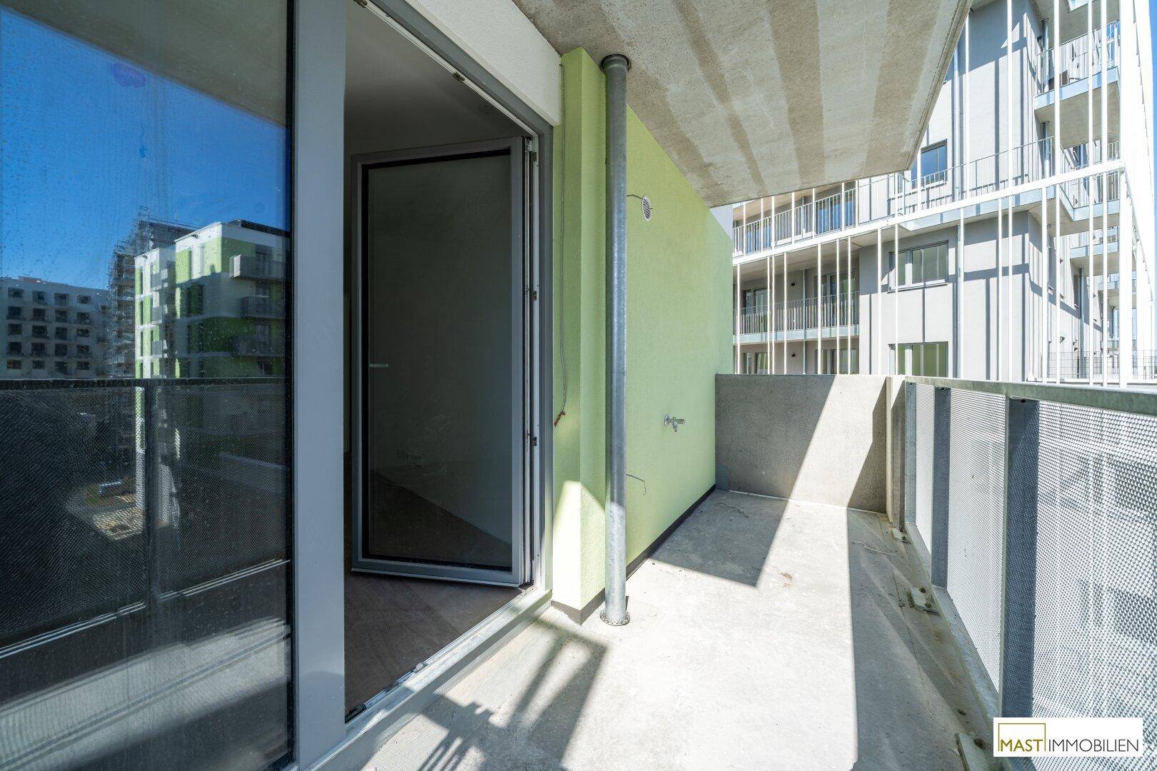 Heller Balkon mit Betonboden und Blick auf die umliegenden Neubauten, ideal für entspannte Stunden.