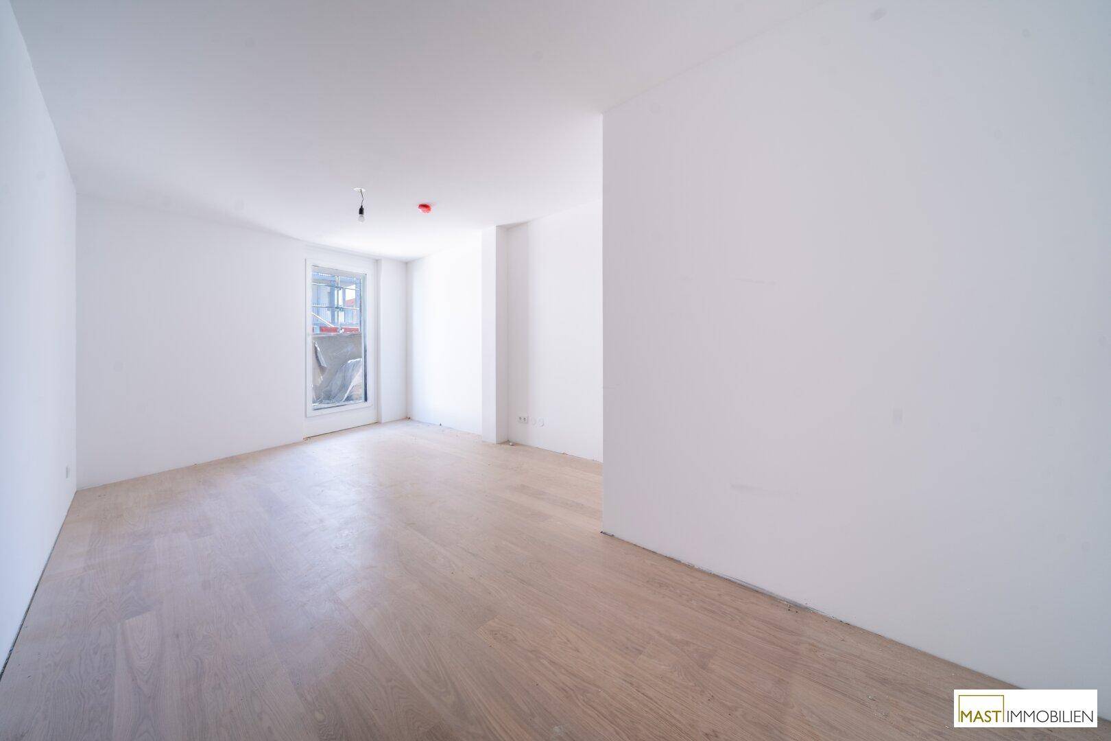 Helles Schlafzimmer mit Parkettboden und Fenster, das viel natürliches Licht hereinlässt.