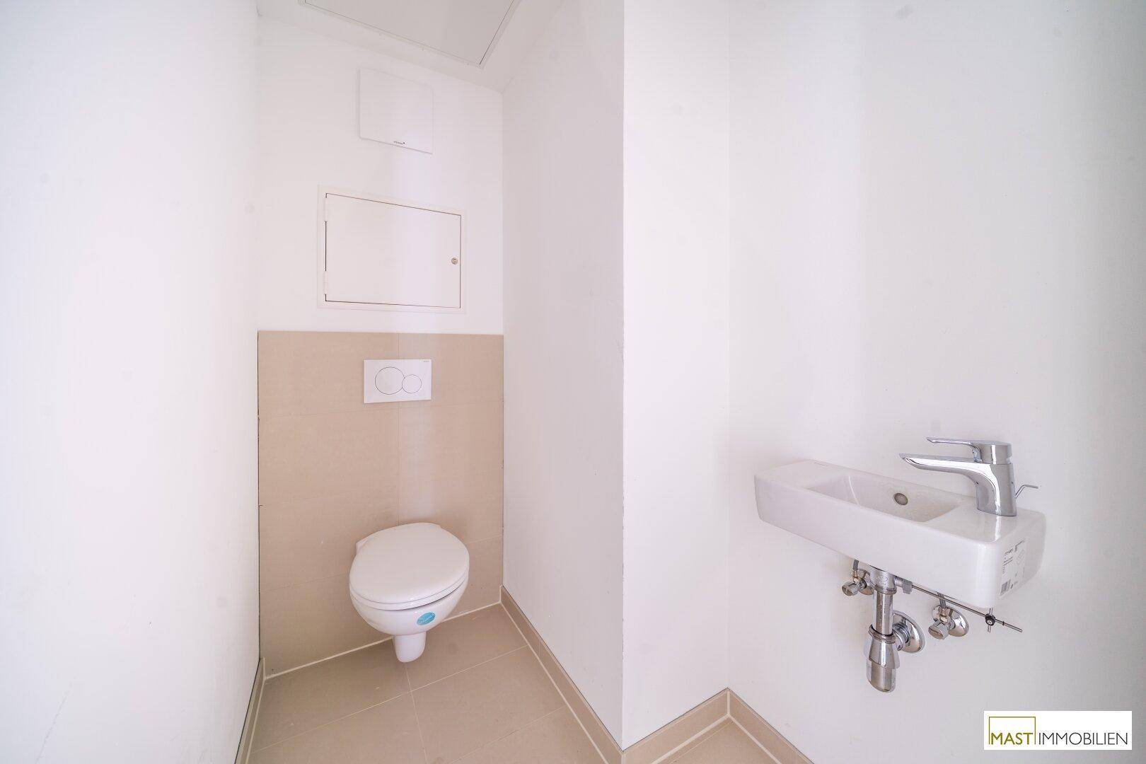 Gäste-WC mit wandhängender Toilette und kleinem Waschbecken, in hellen Farbtönen gehalten.