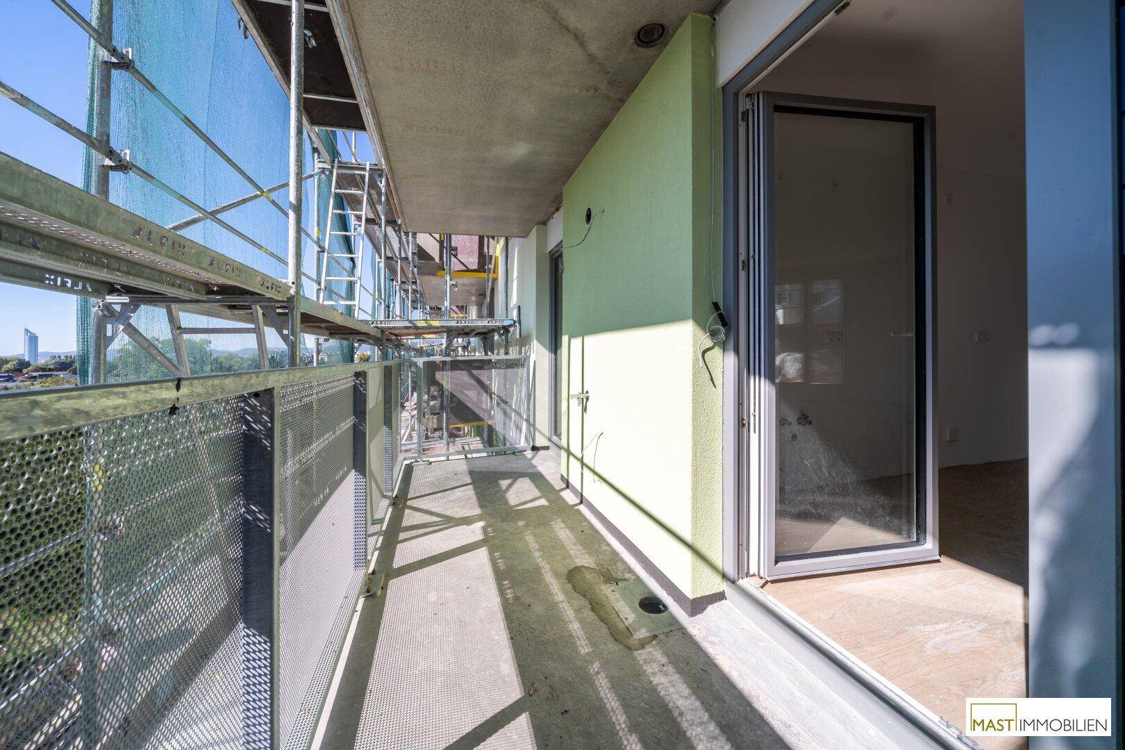 Überdachte Loggia im Bau mit Gerüst und Zugang zum Innenbereich, mit grüner Fassadenfarbe.