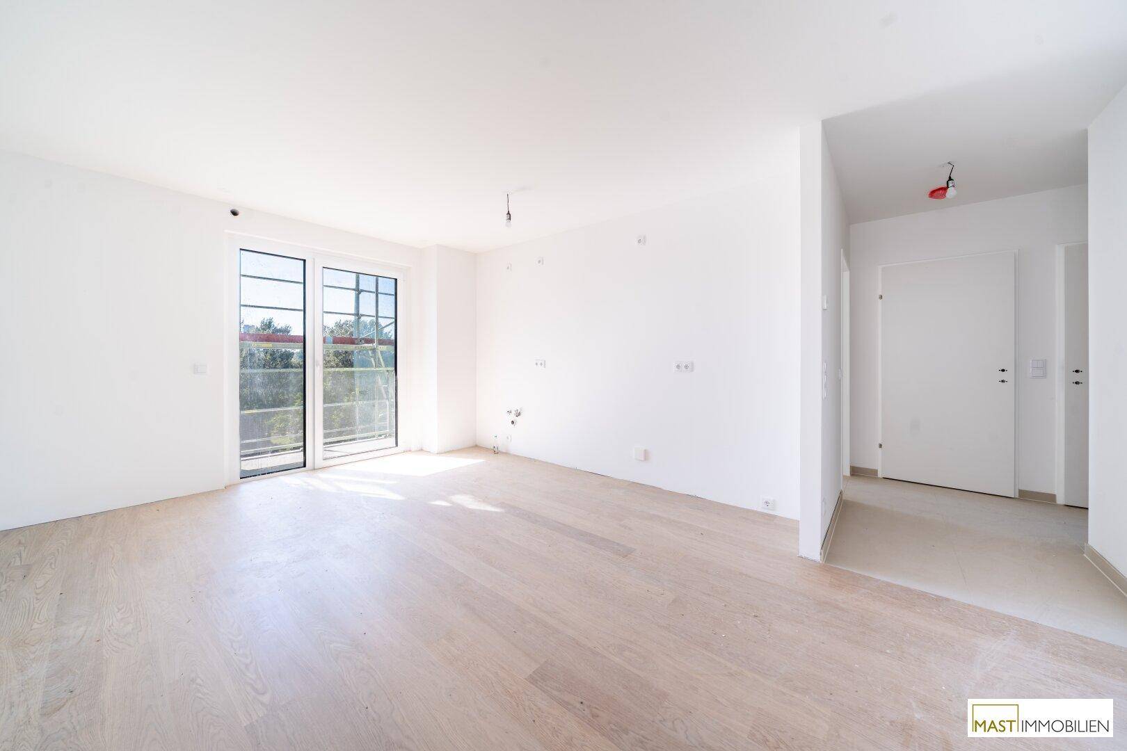 Lichtdurchfluteter Raum mit hellem Parkettboden und Zugang zu einem Außenbereich, ideal als Wohnzimmer.