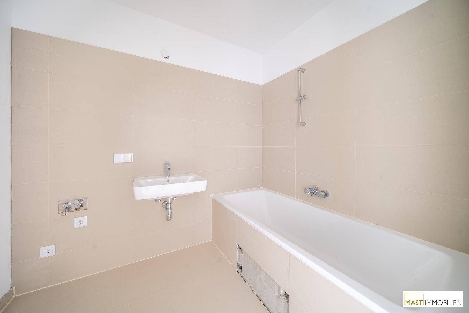 Modernes Badezimmer mit Badewanne, Waschbecken und beigefarbenen Fliesen, in neuwertigem Zustand.