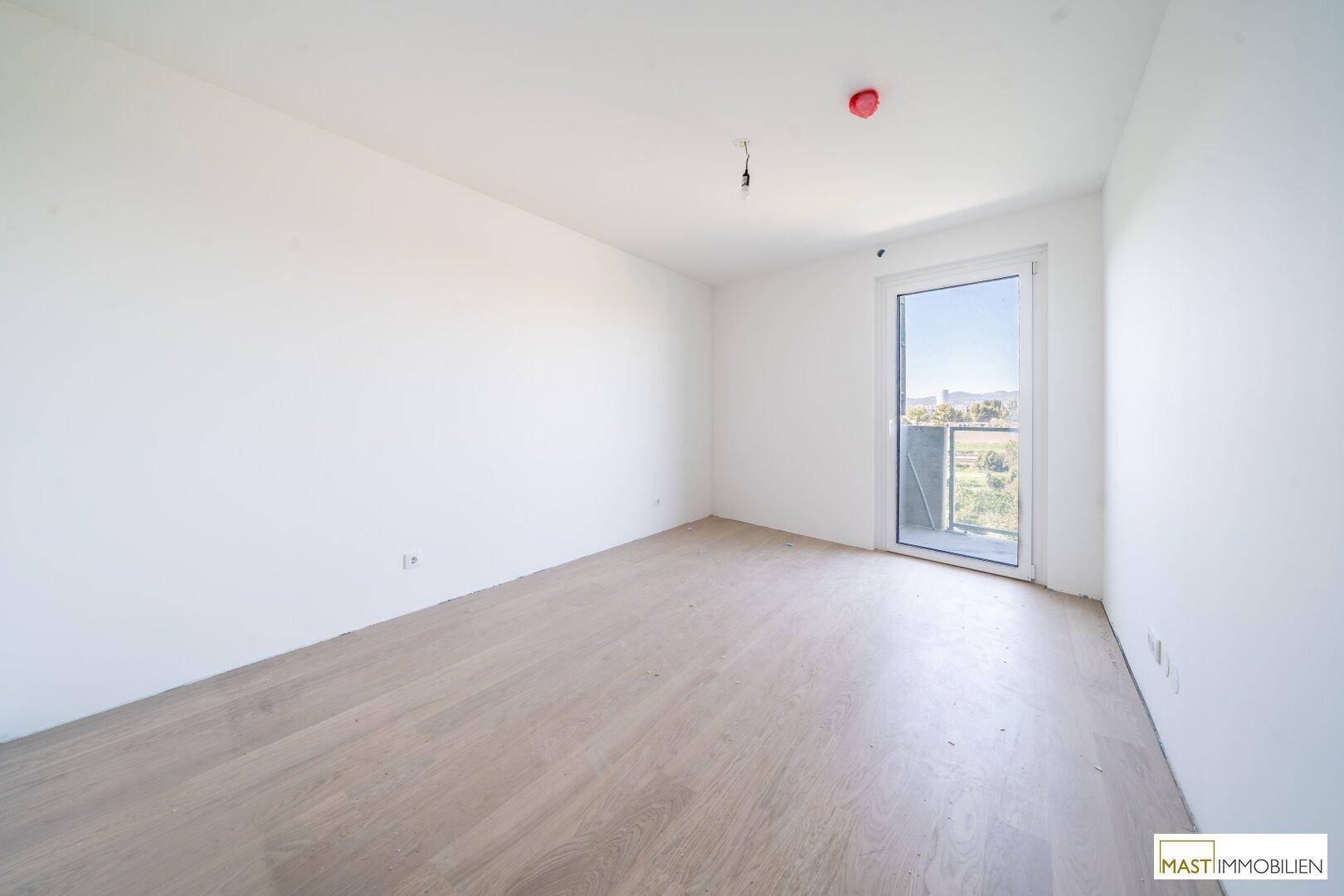 Helles Schlafzimmer mit Parkettboden und Zugang zu einem Balkon, ideal für Neubauwohnungen.