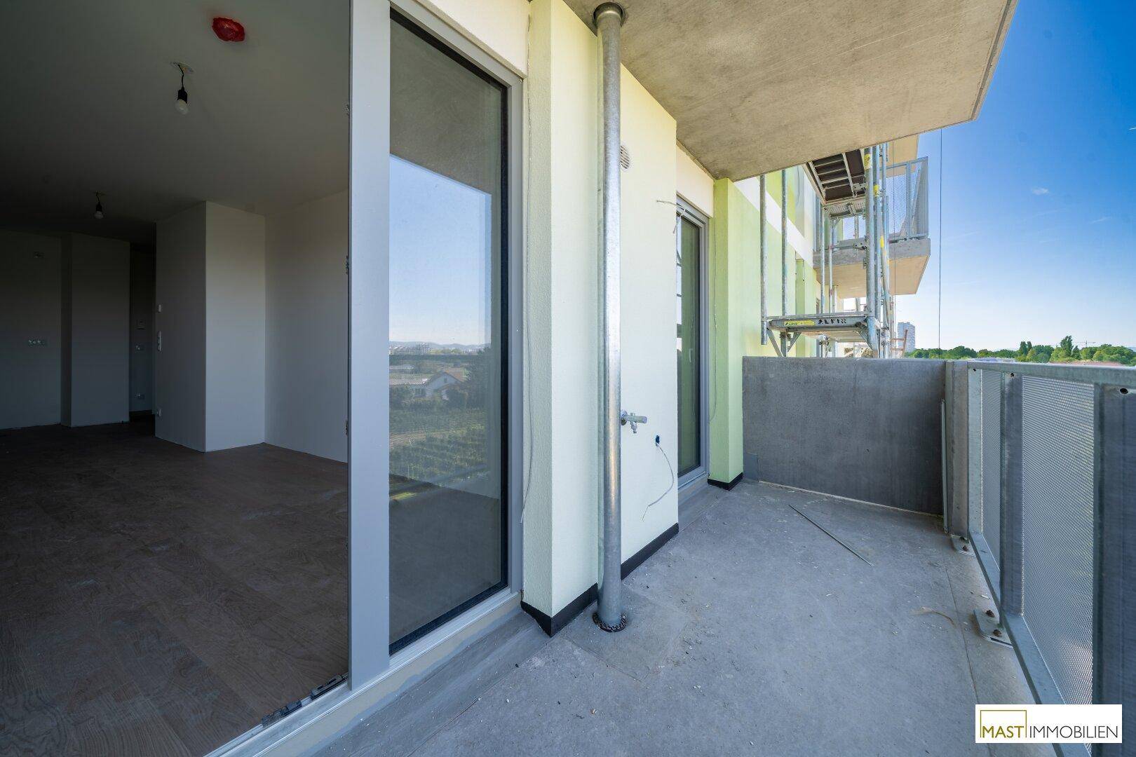 Geräumiger Balkon mit Zugang zum Innenraum und Blick auf die Umgebung, in einem Neubau.