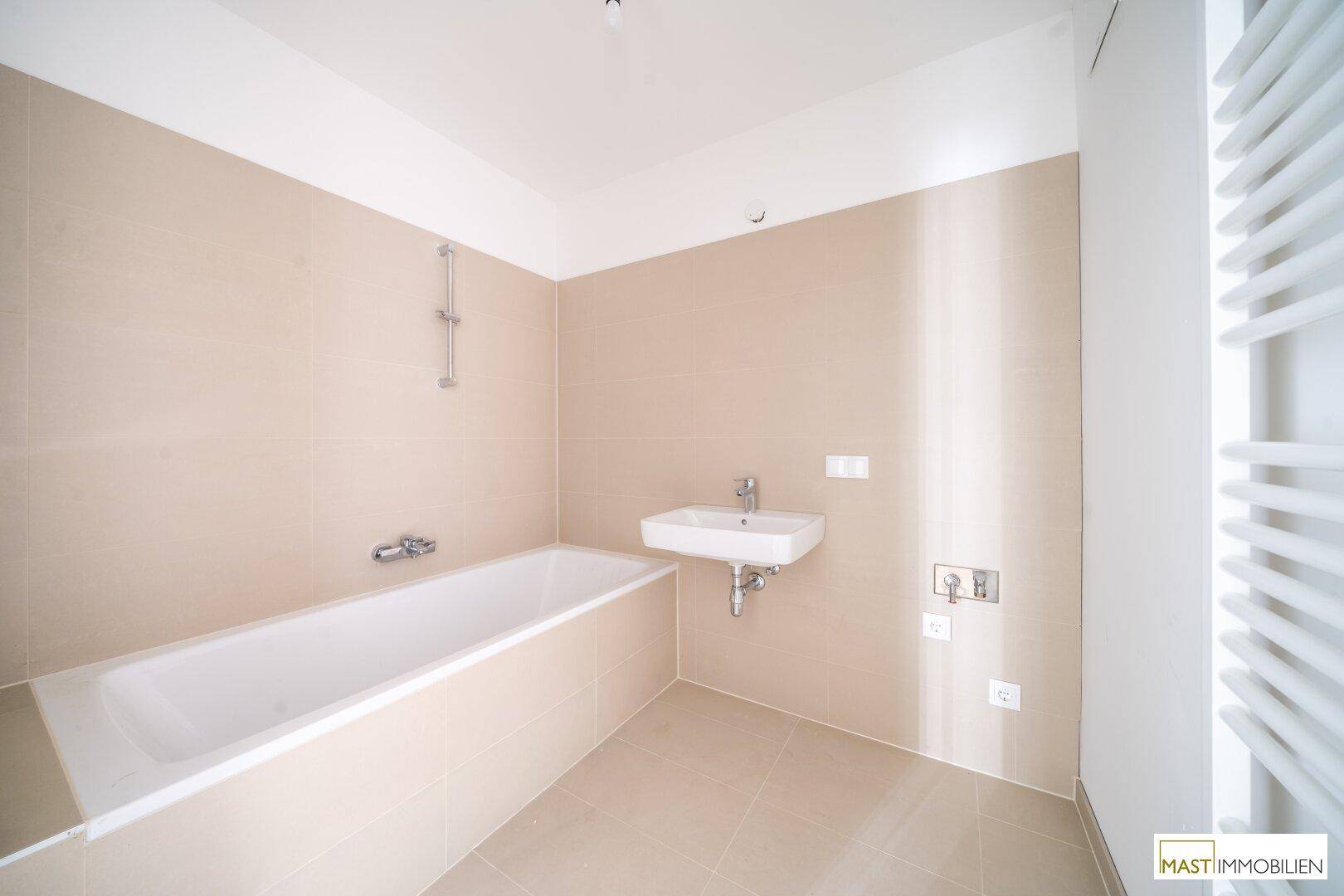 Modernes Badezimmer mit Badewanne, Einzelwaschbecken und beheiztem Handtuchhalter in beigen Fliesen.