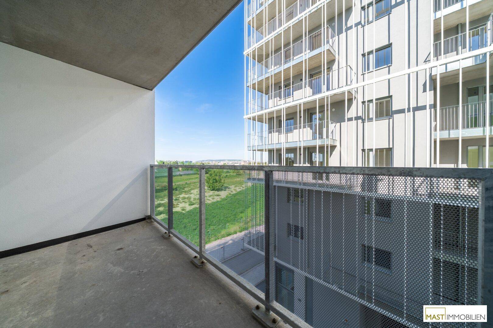 Balkon mit Metallgeländer und weitem Blick über Grünflächen und moderne Wohngebäude.