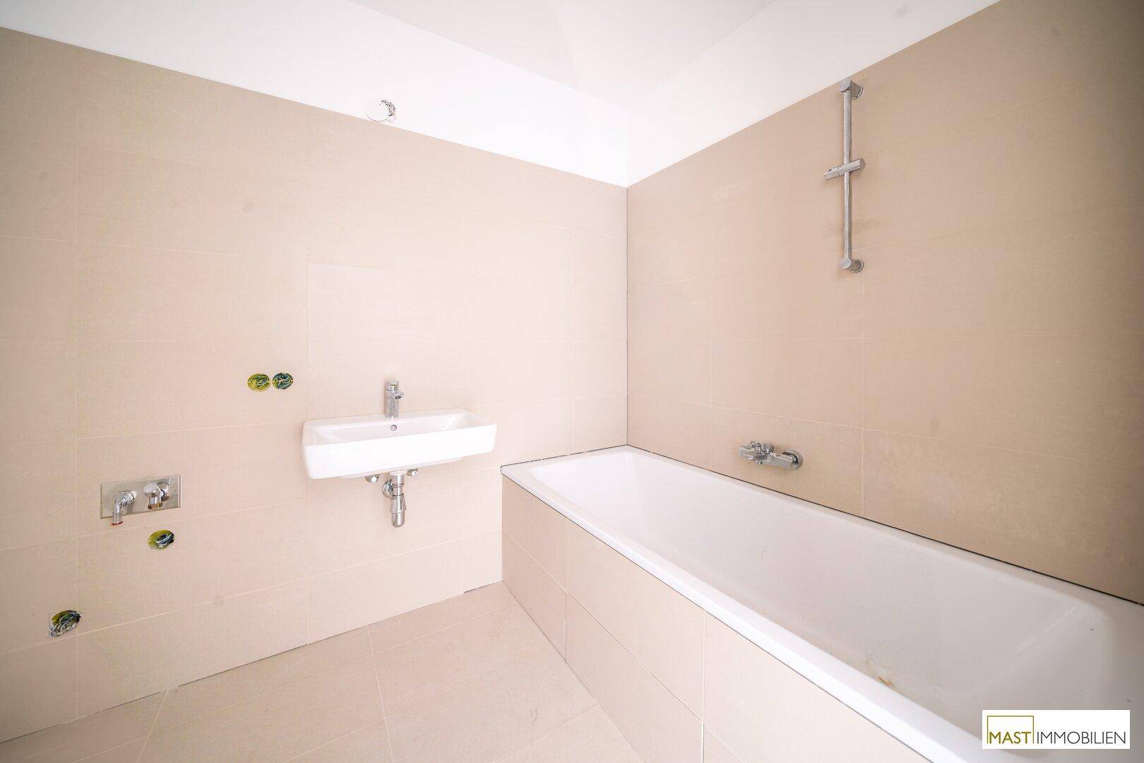 Badezimmer im Bau mit Badewanne, Waschbecken und beigefarbenen Fliesen.