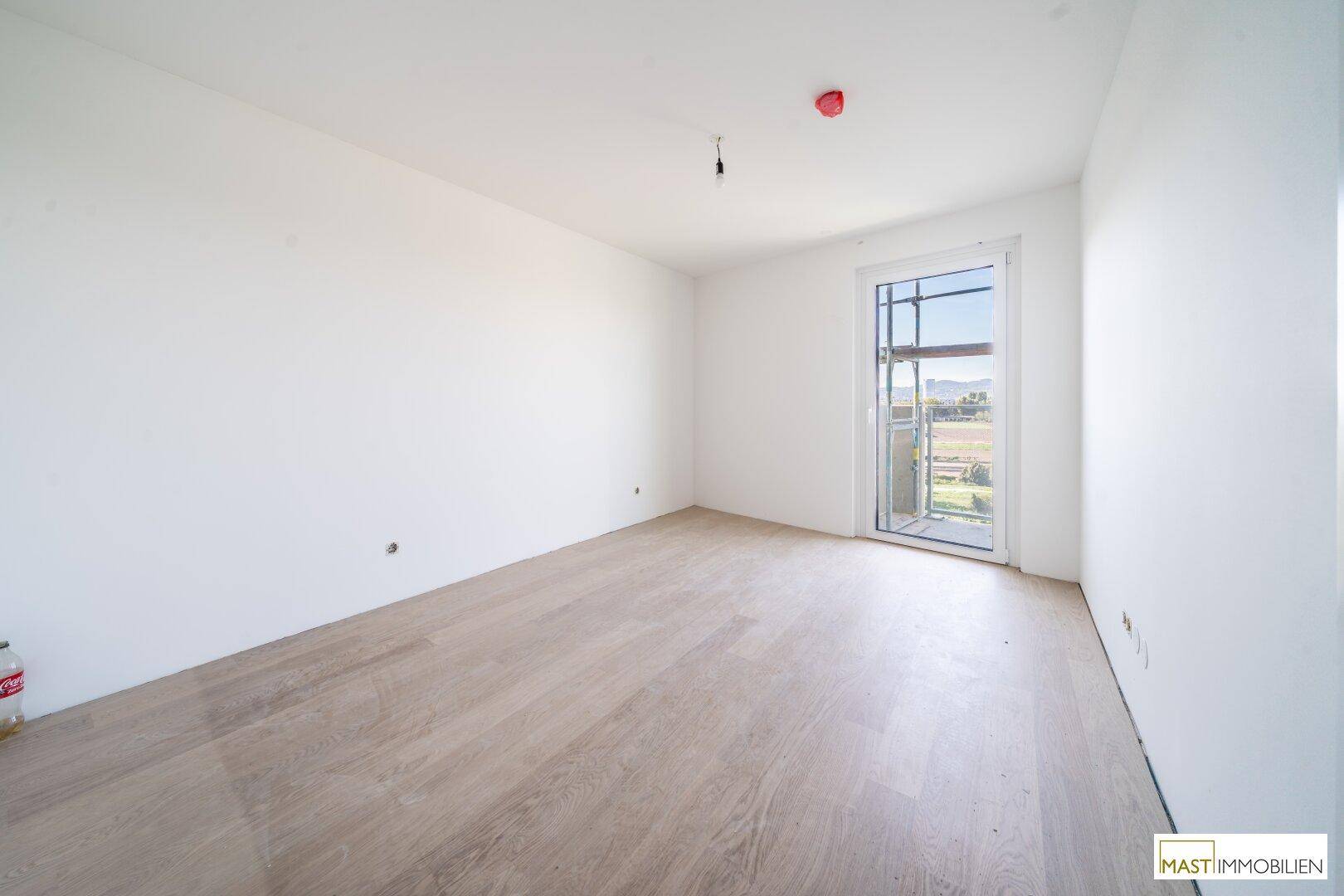 Unmöbliertes Zimmer mit Holzboden und Zugang zu einem Außenbereich mit Gerüst.