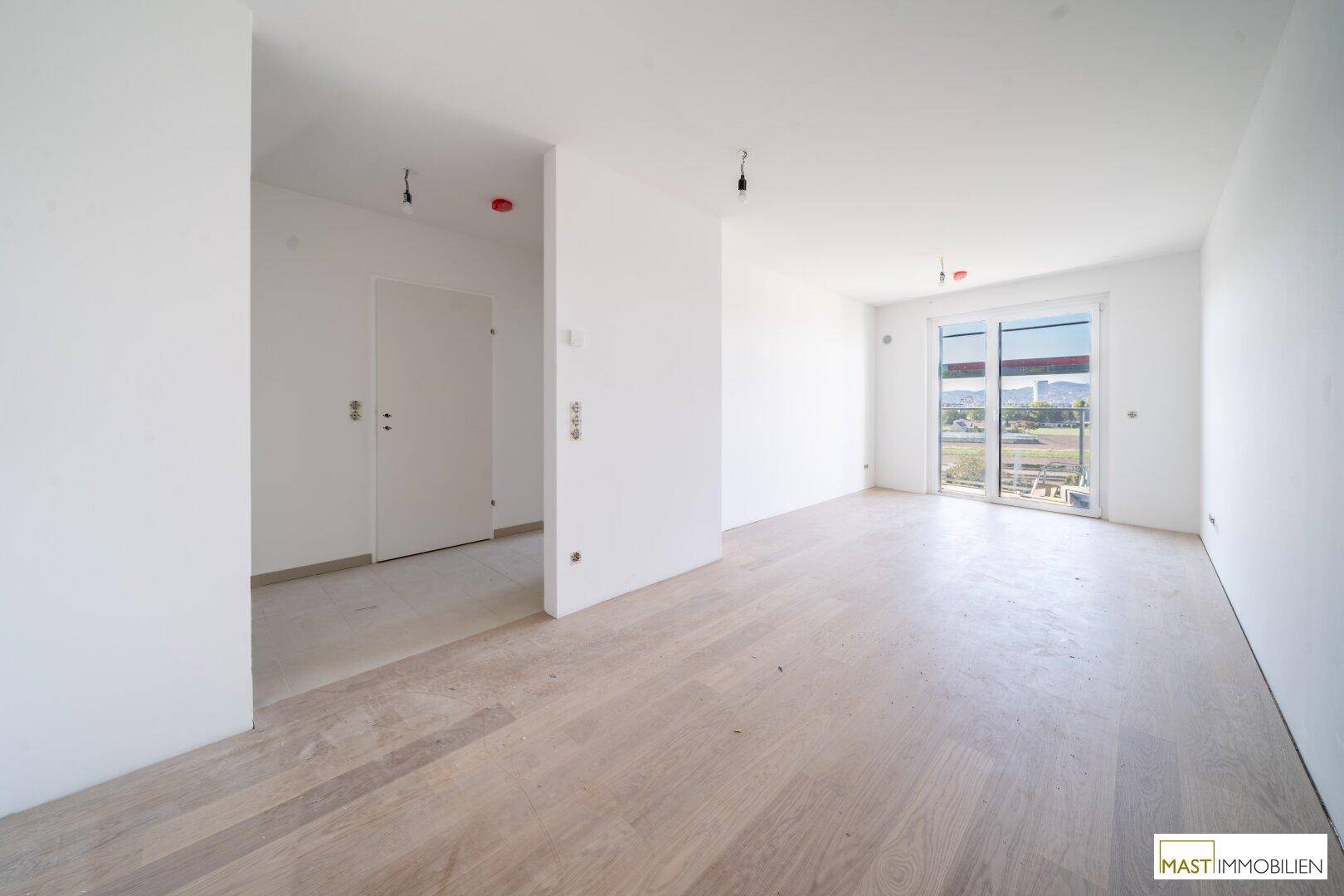Heller, unmöblierter Wohnraum mit hellem Holzboden und Zugang zu einem Balkon.