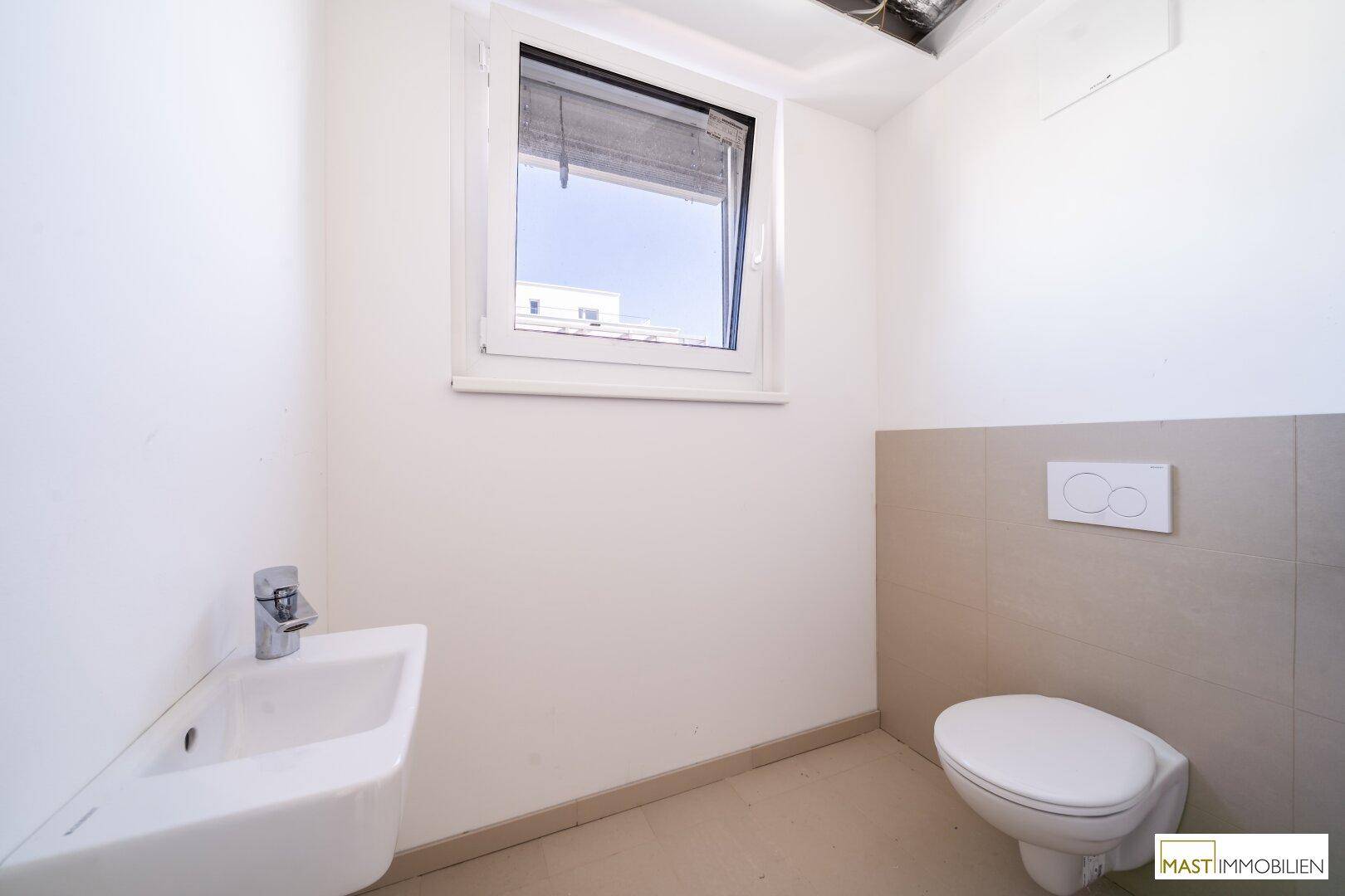 Helles Gäste-WC mit Fenster, wandhängender Toilette und kleinem Waschbecken.