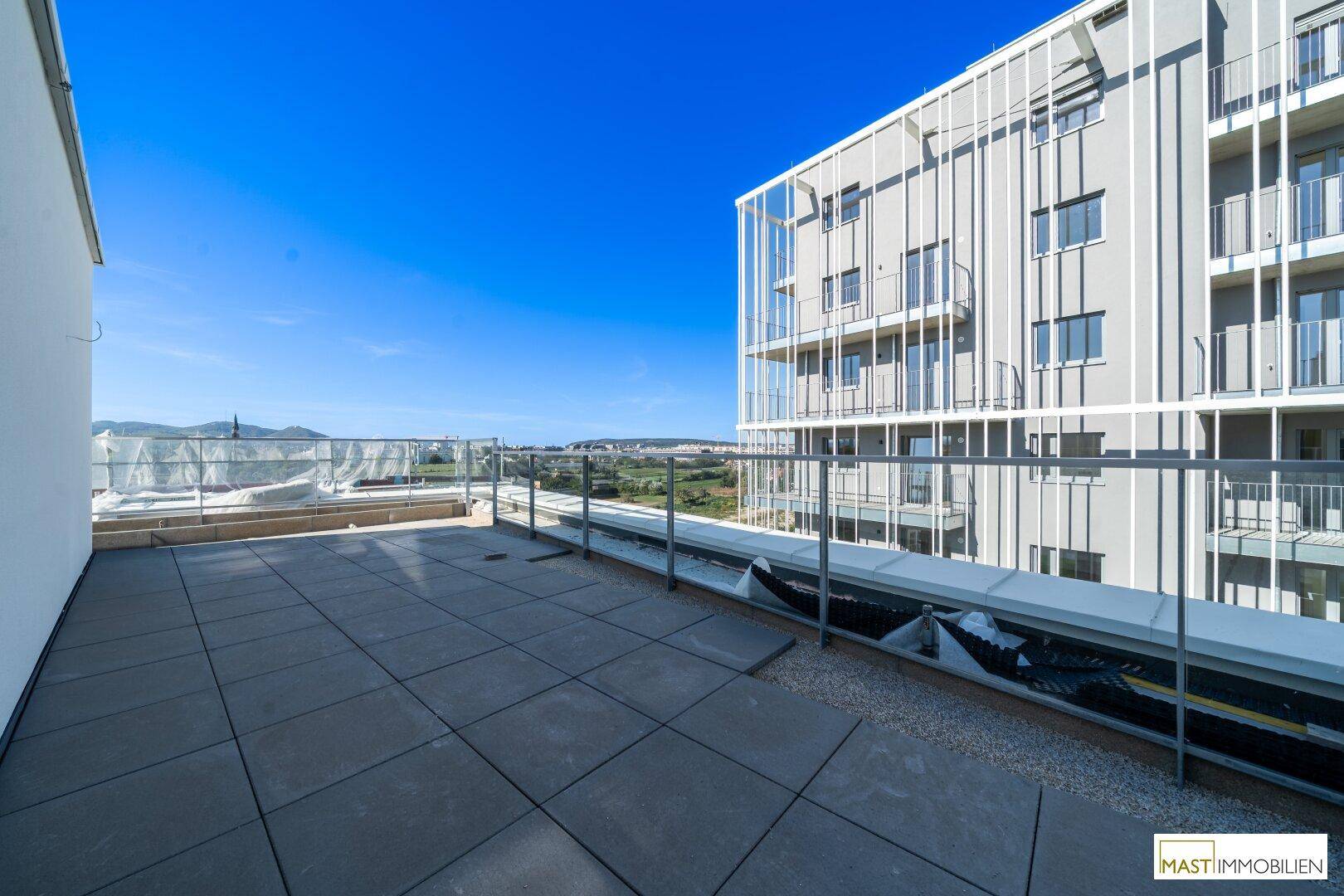 Großzügige Dachterrasse mit Fliesenboden, Glasgeländer und weitem Blick auf die Landschaft.