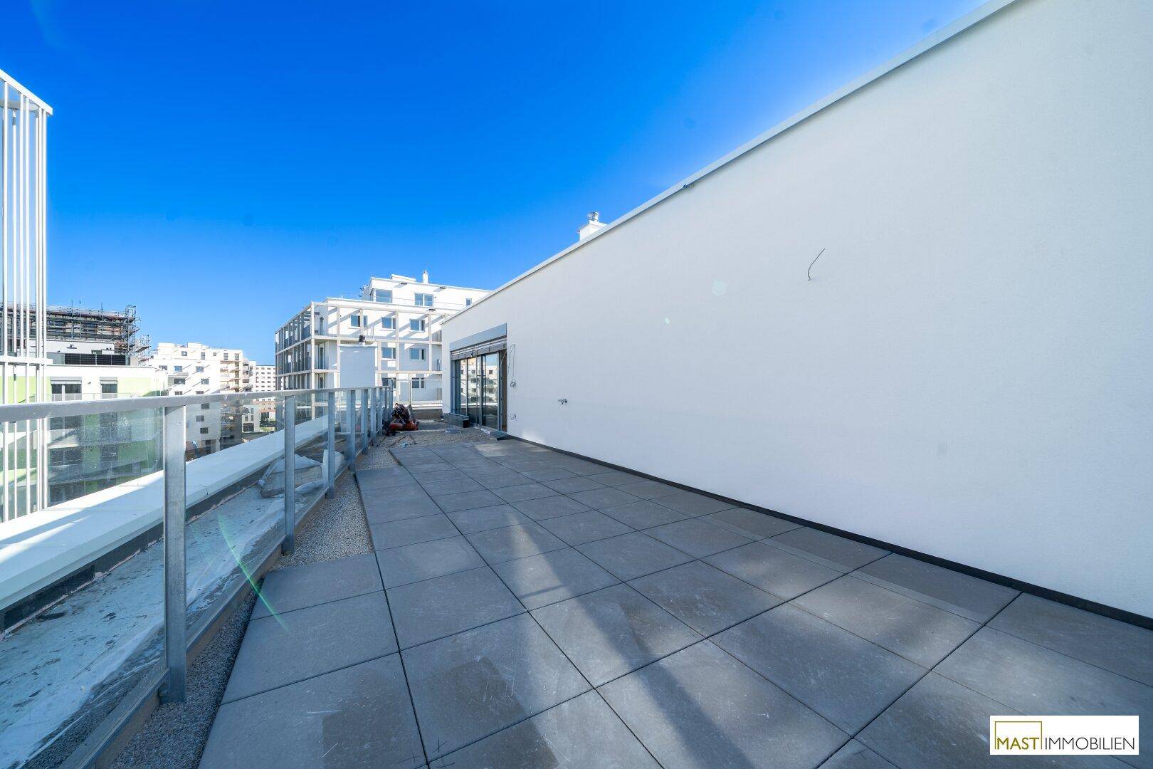 Weitläufige Terrasse mit modernem Fliesenbelag und Blick auf die umliegenden Neubauten.