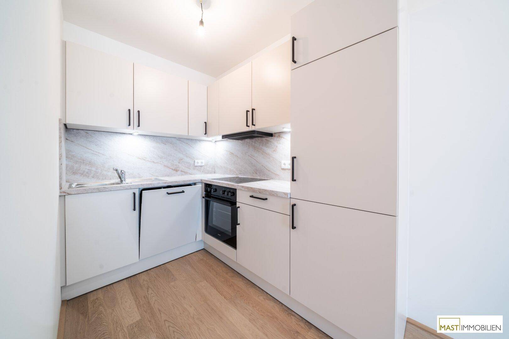 Moderne Einbauküche mit weißen Schränken, integrierten Geräten und heller Arbeitsplatte in neuwertigem Zustand.