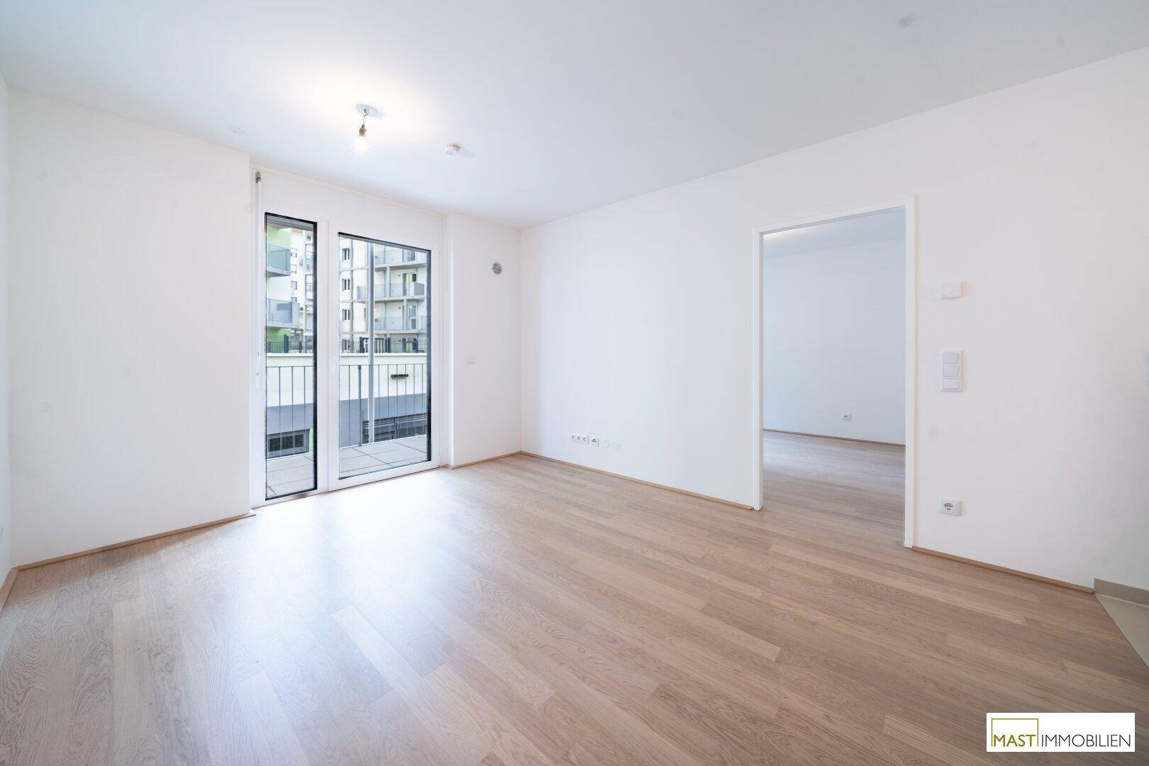 Geräumiges Wohnzimmer mit hellem Laminatboden, großen Fenstern und direktem Zugang zum Balkon.