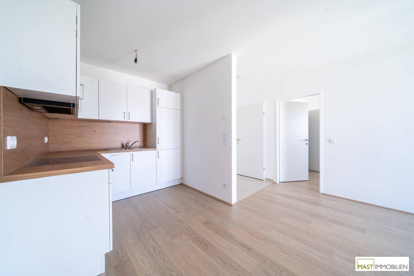 Moderne Küchenzeile mit weißen Schränken, Holz-Arbeitsplatte und hellem Parkettboden.