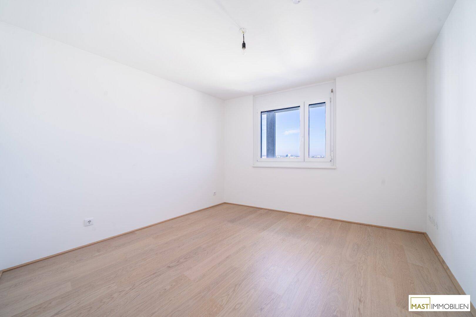 Helles Schlafzimmer mit Parkettboden und einem Fenster, das viel Tageslicht hereinlässt.
