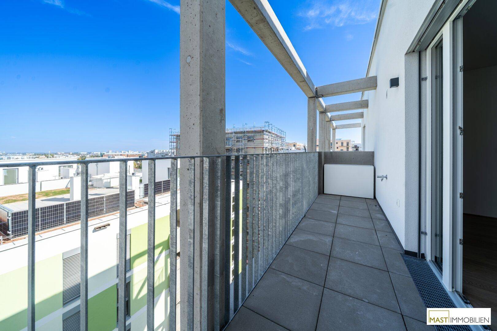 Geräumiger Balkon mit Fliesenboden und Zugang vom Innenbereich, umgeben von moderner Architektur.