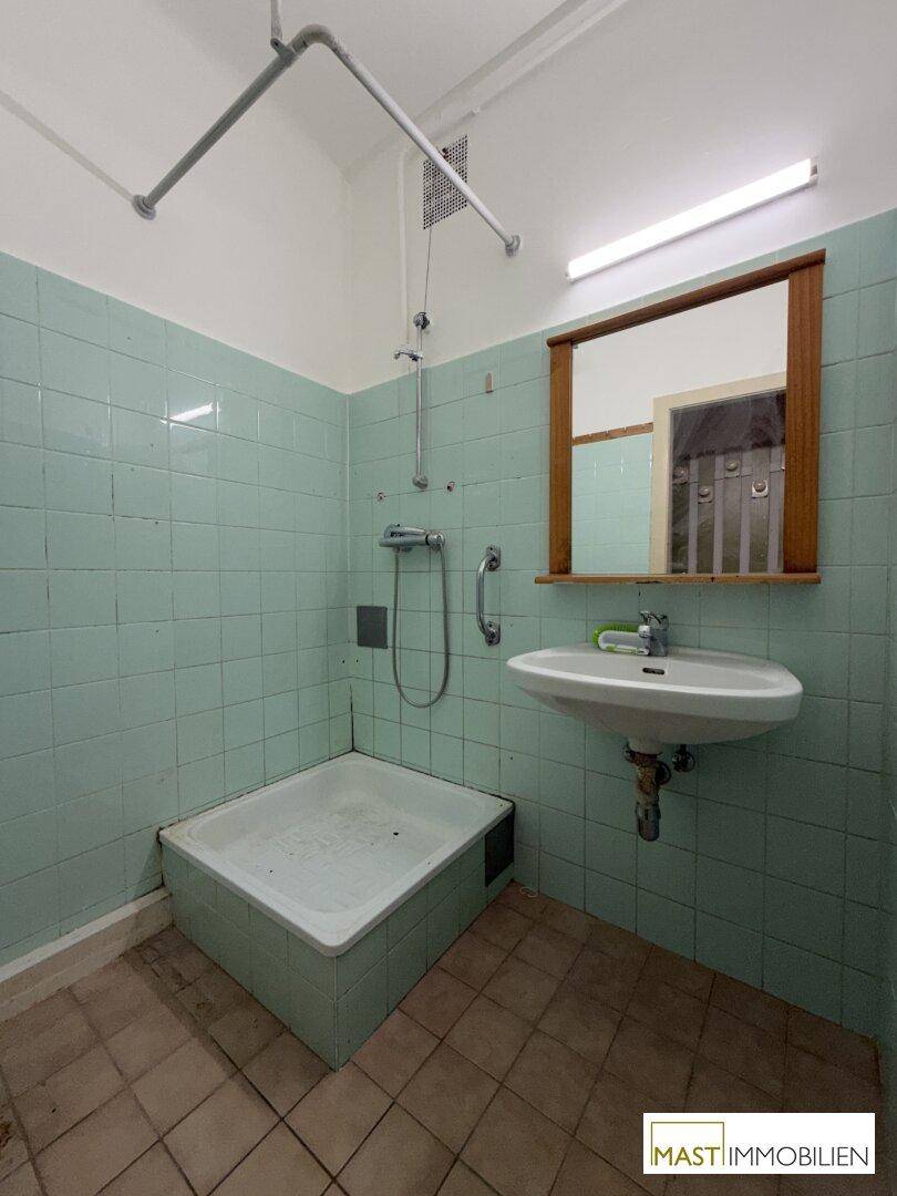 Badezimmer mit mintgrünen Fliesen, Duschwanne und einem Waschbecken mit Spiegel.