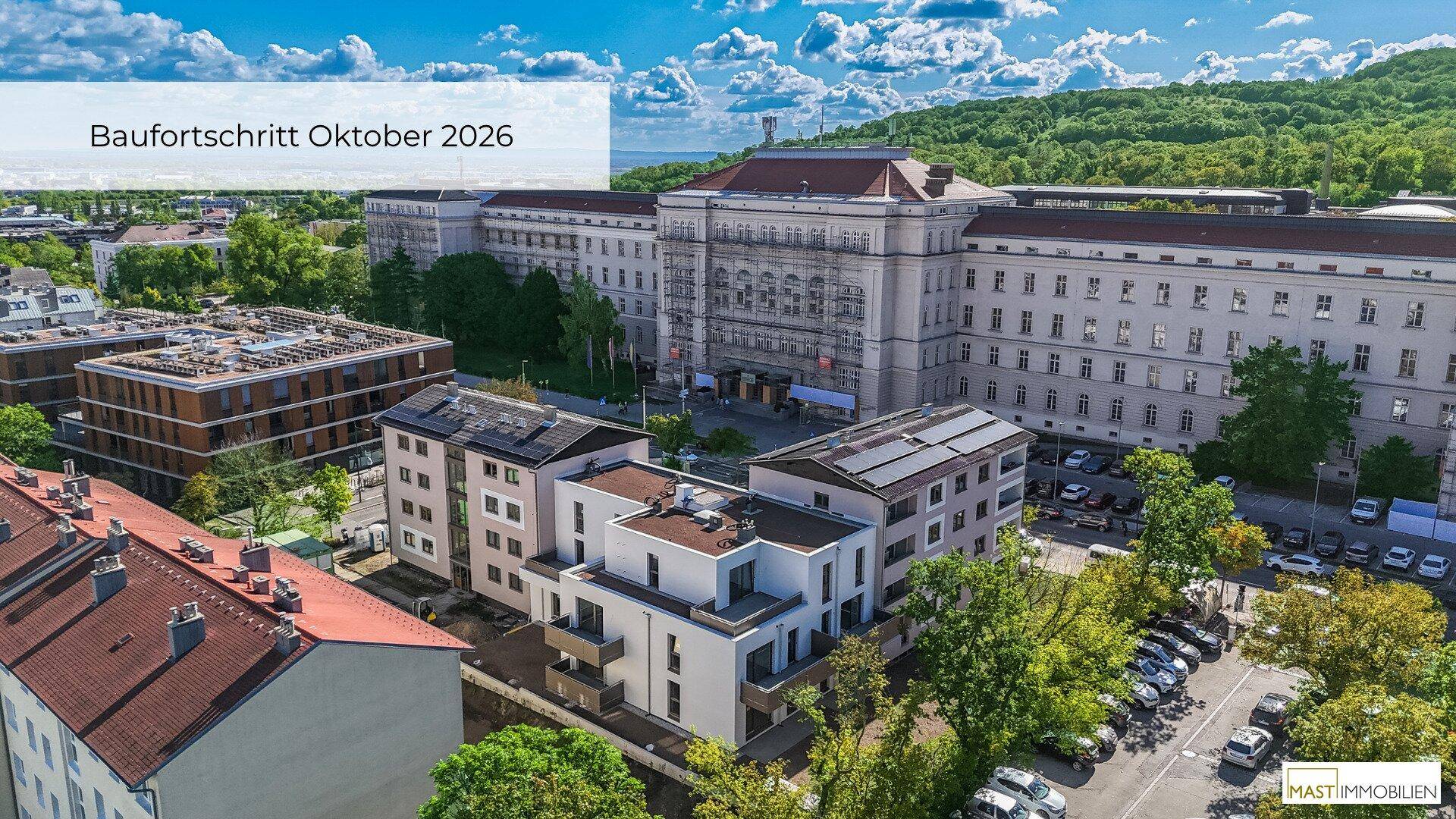 Weitläufige Luftaufnahme eines Wohnkomplexes mit umliegenden Gebäuden, Parkplätzen und Grünflächen.