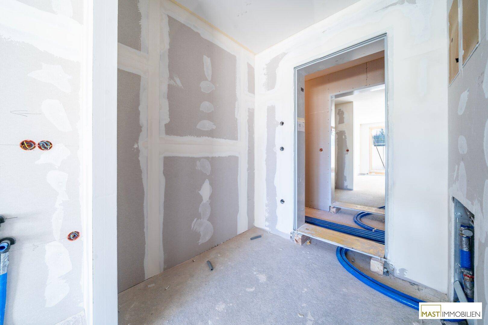 Unfertiger Flurbereich mit Trockenbauwänden und vorbereiteten Leitungen für die weitere Installation.