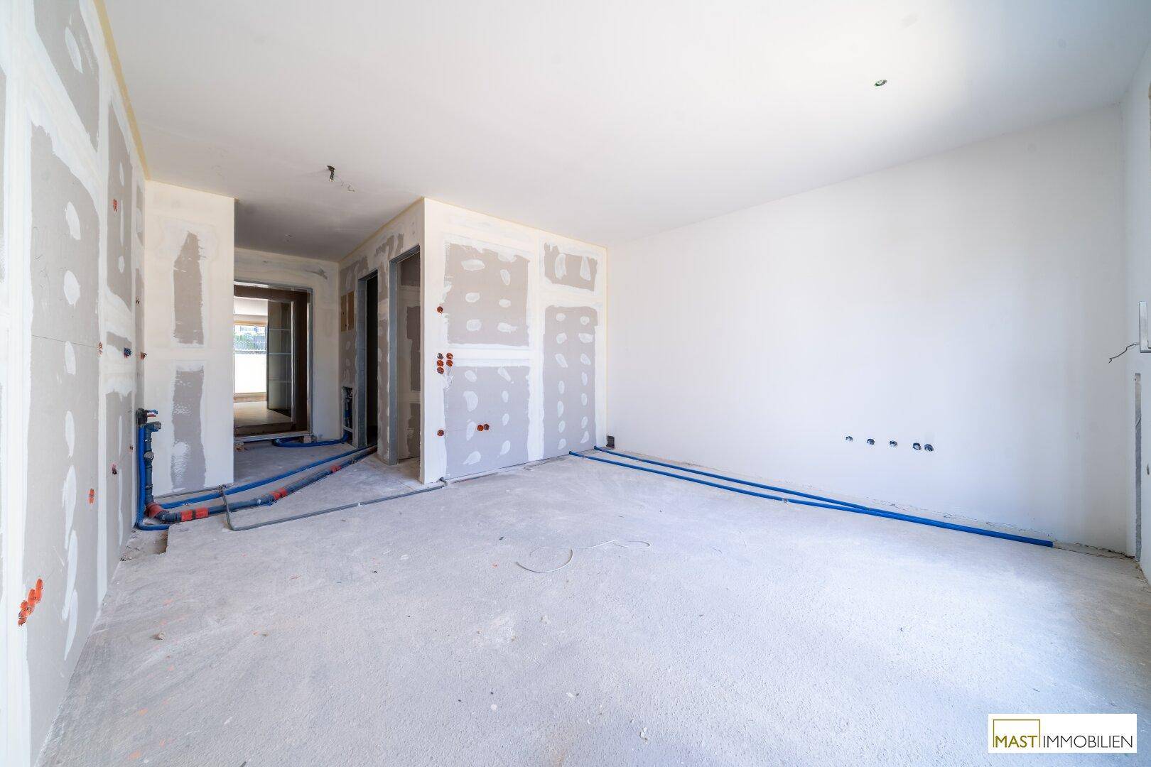 Rohbau-Innenraum mit sichtbaren Installationen und Durchgang zu weiteren Zimmern.