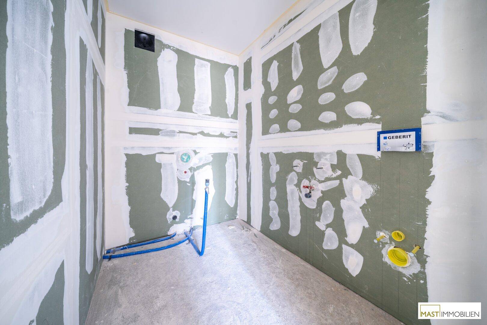 Badezimmer im Rohbau mit sichtbaren Wasseranschlüssen und vorbereiteten Wänden für die Installation.
