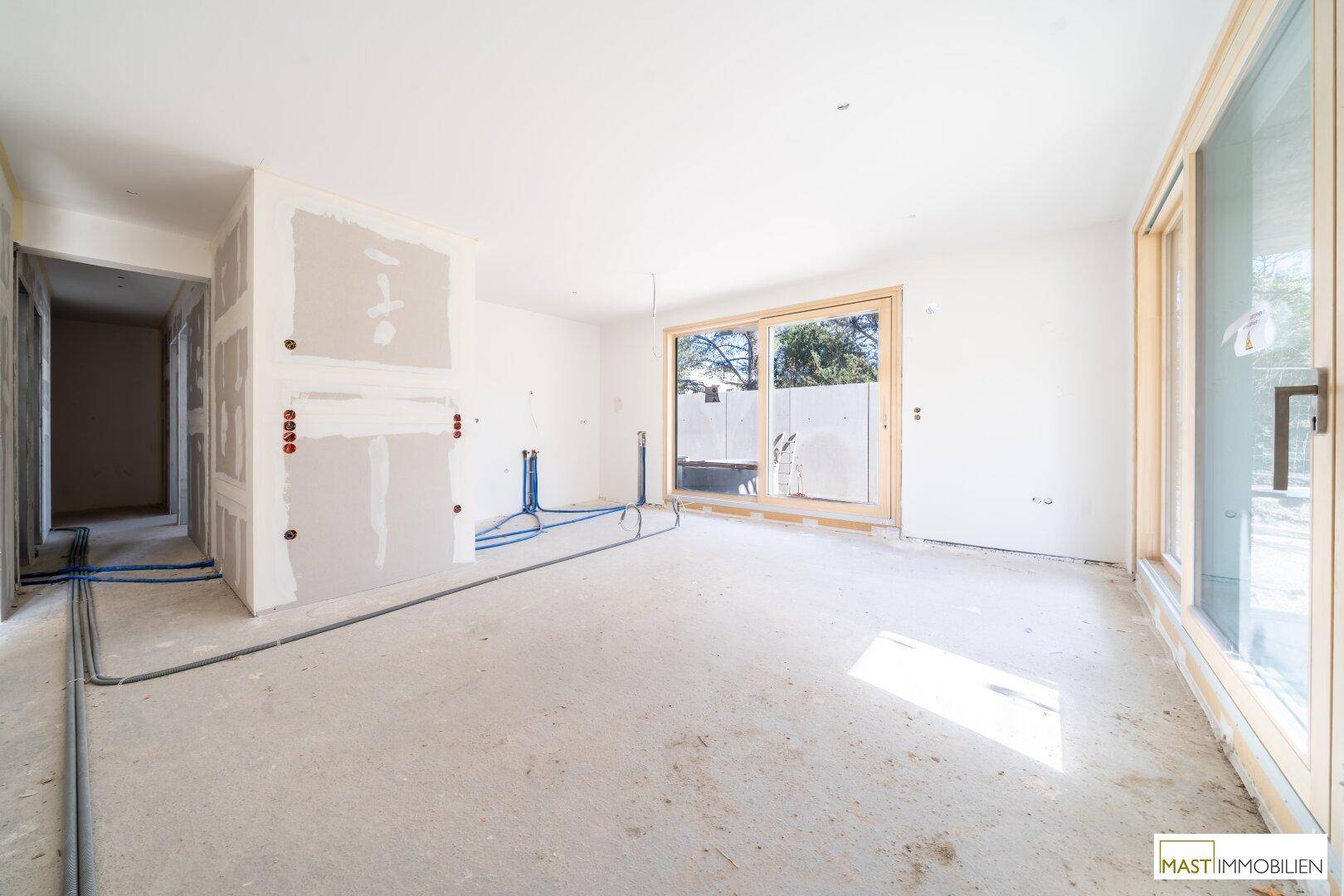 Heller Innenraum im Rohbau mit großen Fenstern und sichtbaren Installationen, bereit für den Ausbau.