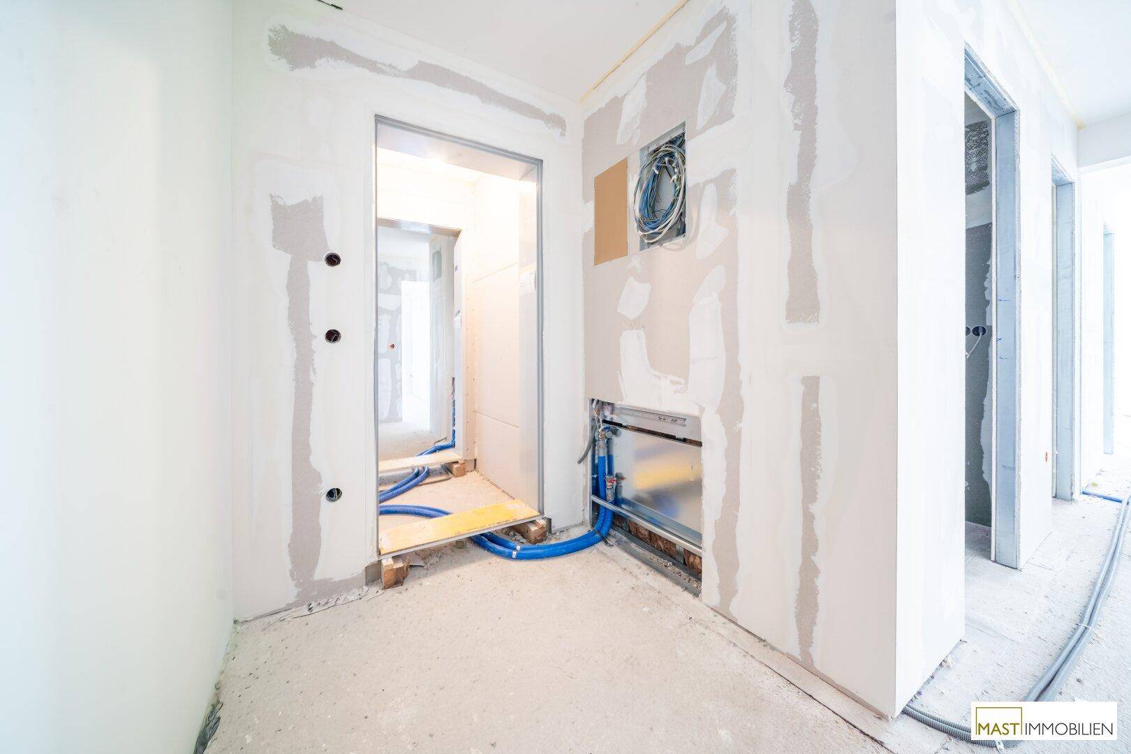 Baustelle im Innenbereich mit sichtbaren Installationen und Türrahmen, deutet auf einen zukünftigen Funktionsraum hin.