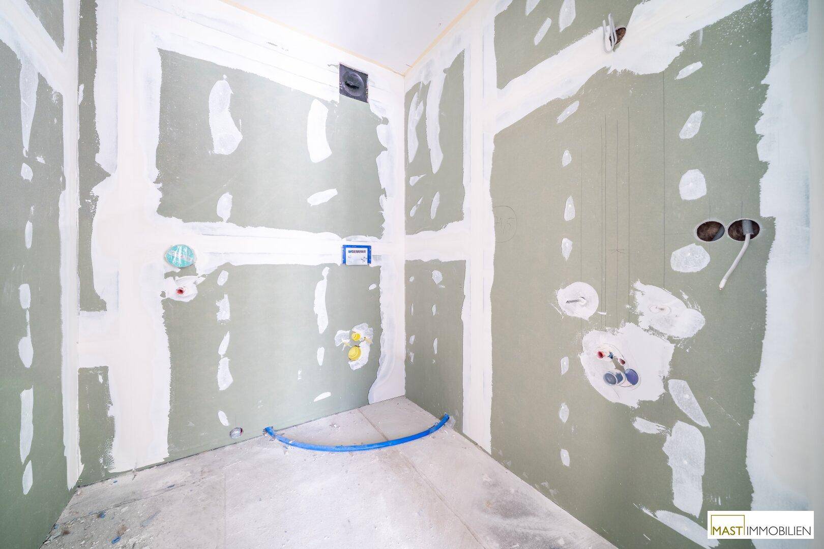 Badezimmer im Rohbau mit vorbereiteten Anschlüssen für Sanitäranlagen und Trockenbauwänden.