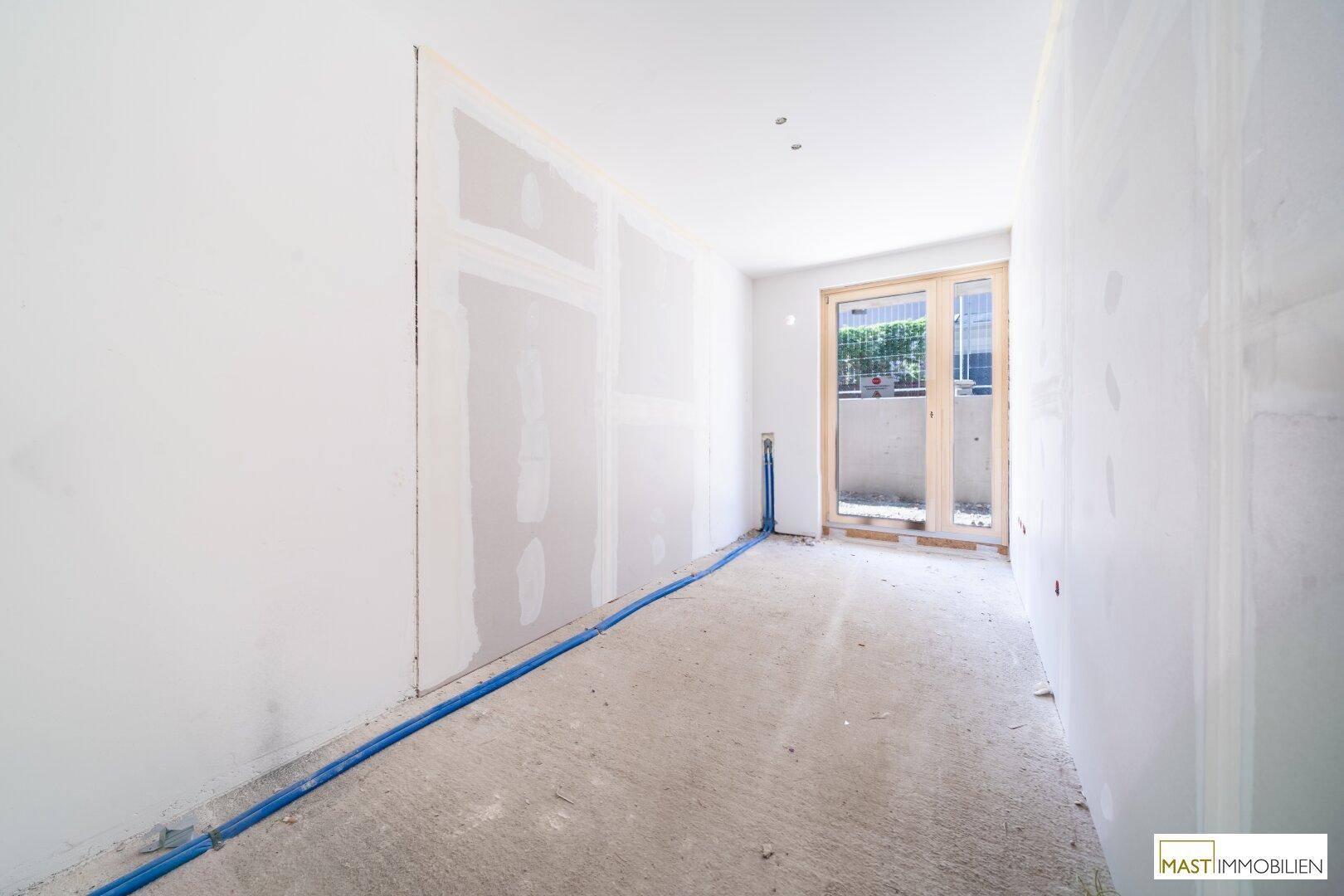 Unfertiger Raum mit sichtbaren Installationen und Betonboden, bereit für den weiteren Innenausbau.