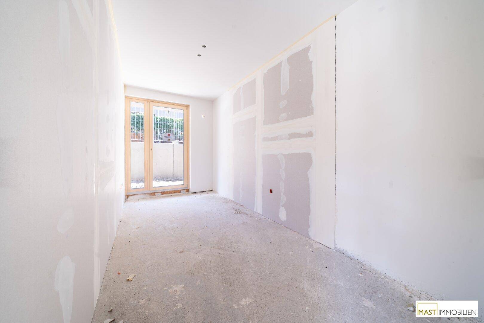 Unfertiger Raum im Neubau mit Betonboden und einer Tür, die ins Freie führt, bereit für den Ausbau.