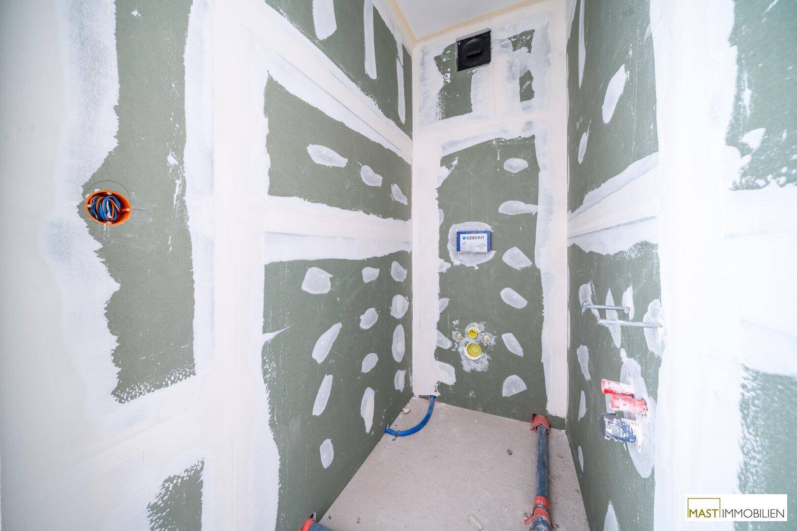Kleiner Raum im Rohbau mit Trockenbauwänden und vorbereiteten Anschlüssen für ein Wand-WC.