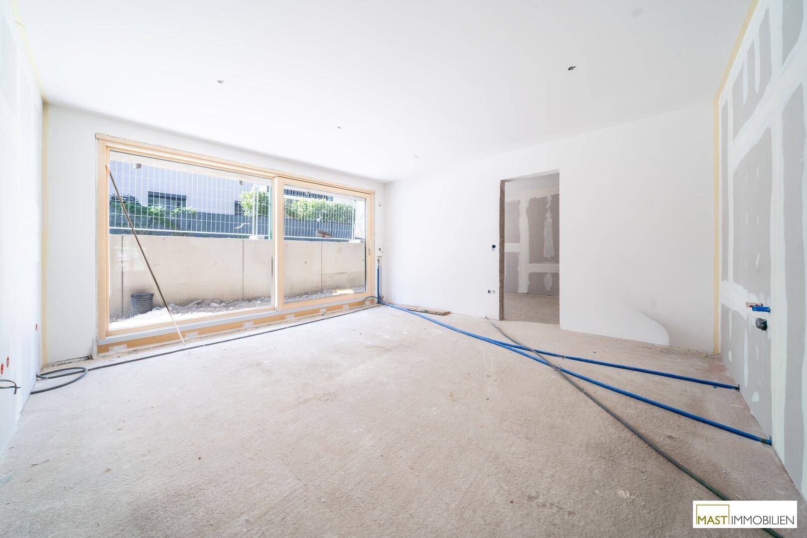 Heller Innenraum im Rohbau mit großen Schiebetüren und vorbereiteten Installationen für den Innenausbau.