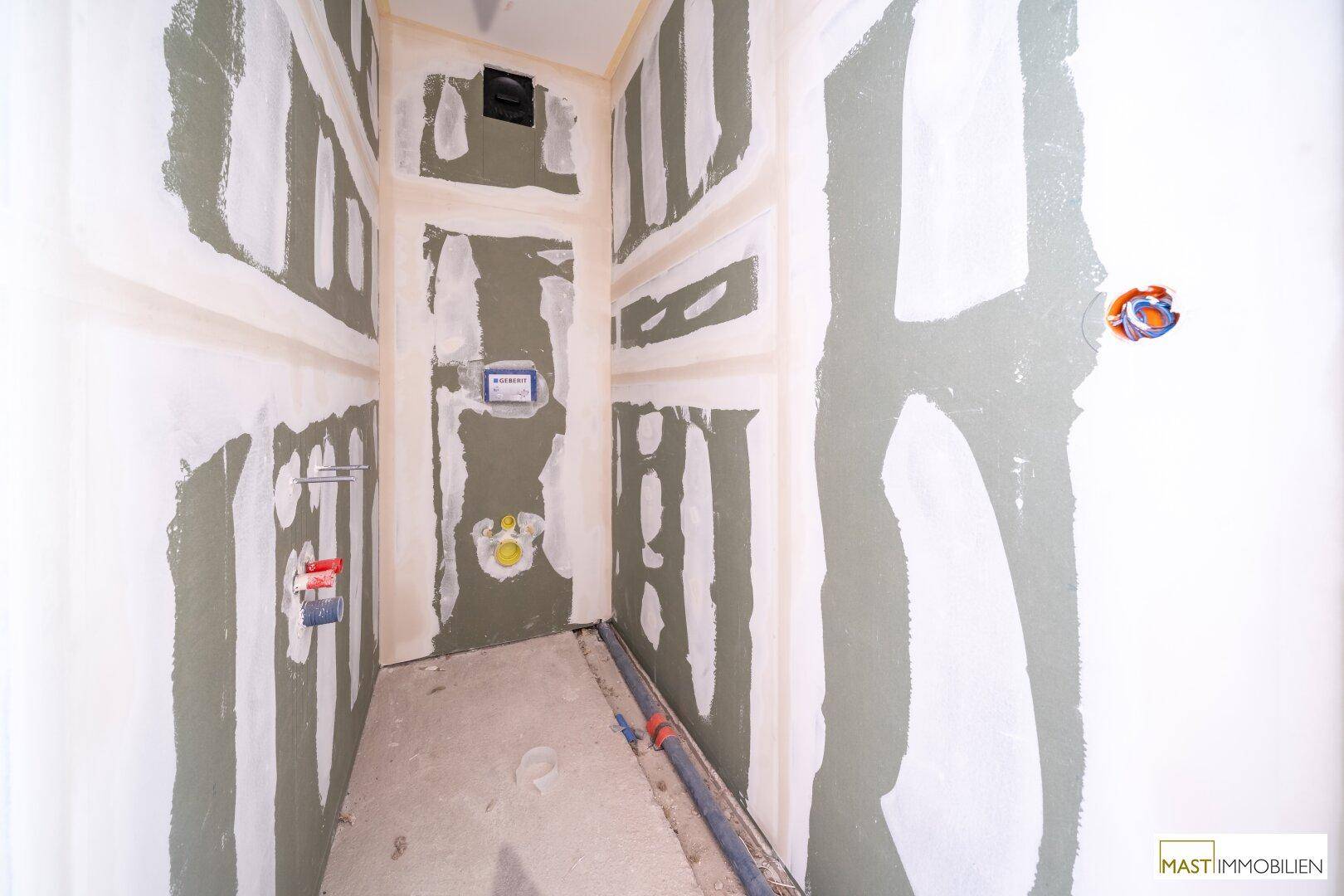 Rohbau-Badezimmer oder WC mit grünen Trockenbauwänden und sichtbaren Sanitärinstallationen.