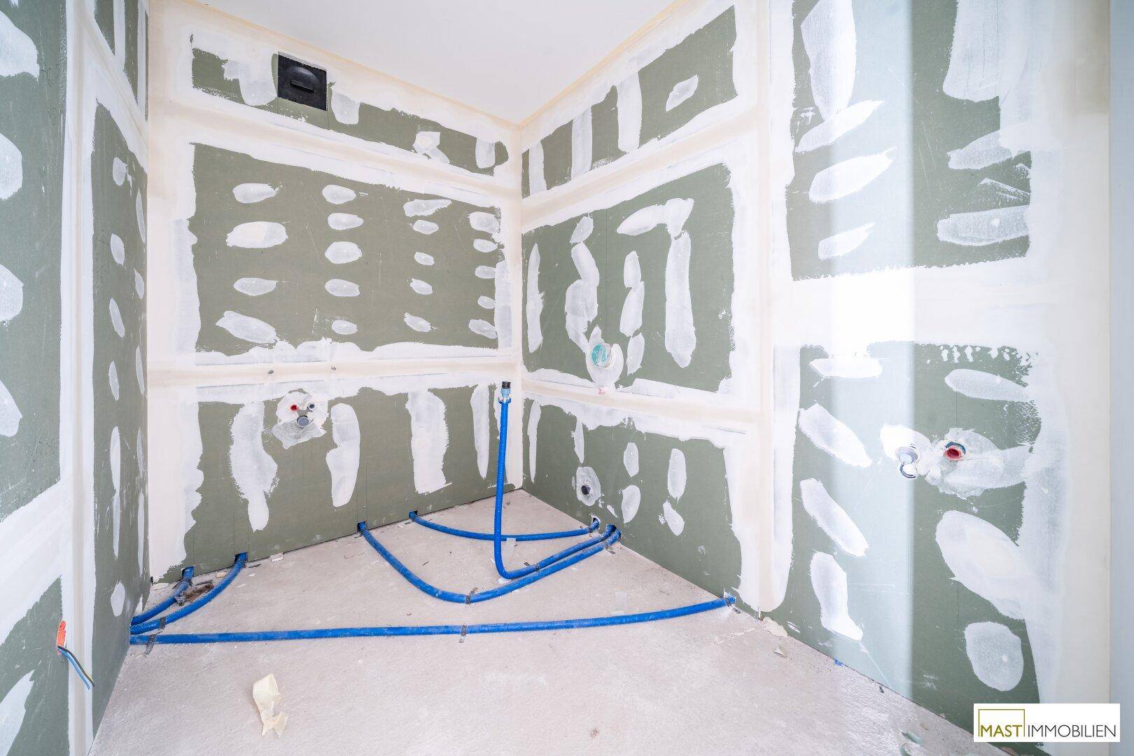 Rohbau-Badezimmer mit grünen Trockenbauwänden und vorbereiteten Anschlüssen für Sanitäranlagen.