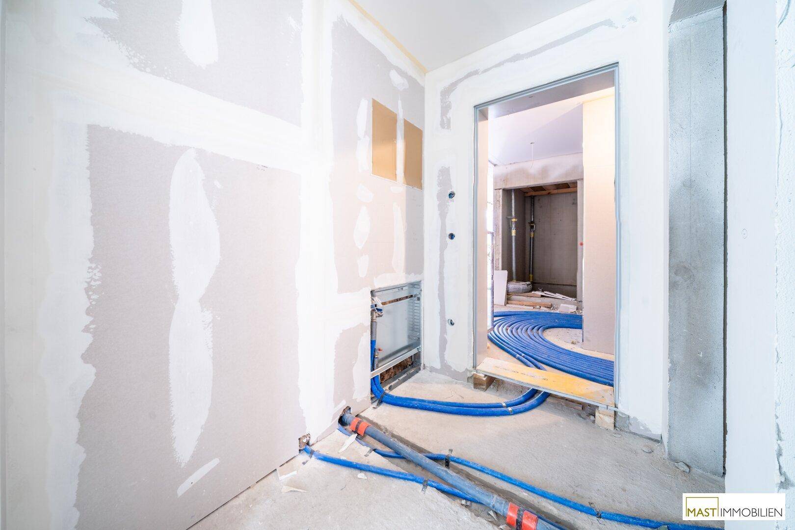 Rohbau-Innenraum mit sichtbaren blauen Leitungen und Vorbereitungen für Installationen.