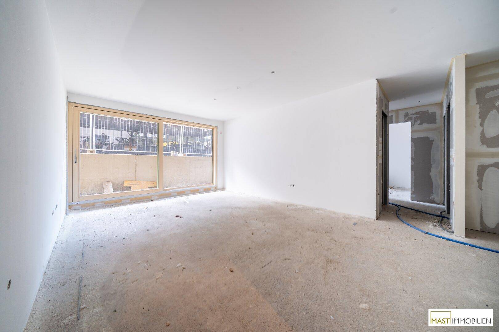 Unfertiger Innenraum mit großen Fenstern und Betonboden während der Bauphase.