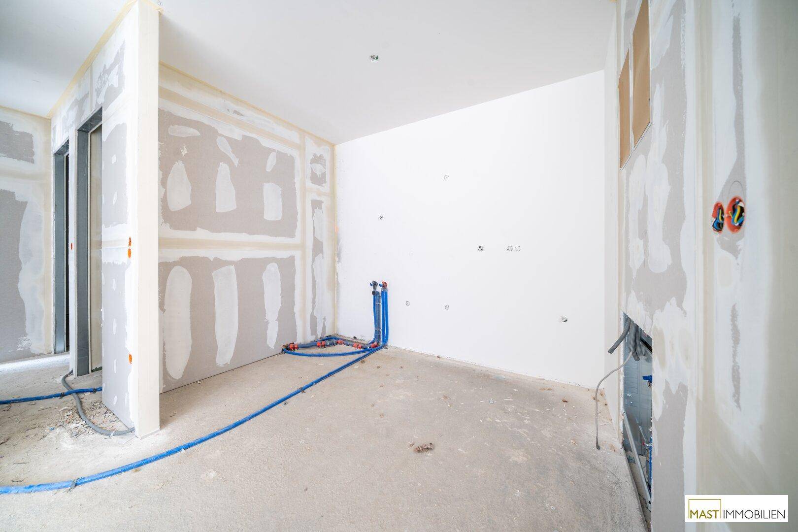 Innenraum im Rohbau mit Trockenbauwänden, Betonboden und sichtbaren Installationen.