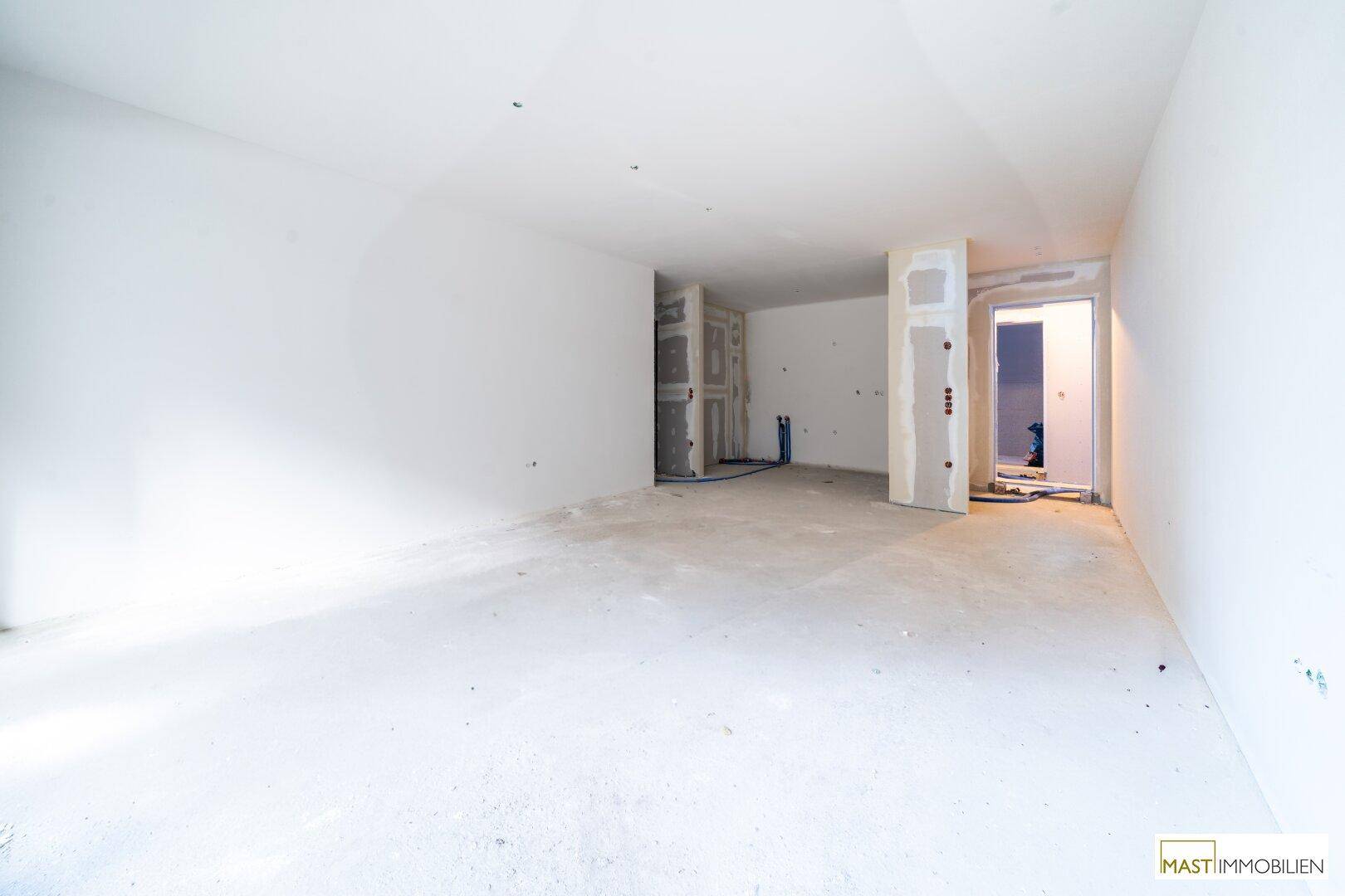 Geräumiger, unfertiger Innenraum mit Betonboden und vorbereiteten Wänden für den weiteren Ausbau.