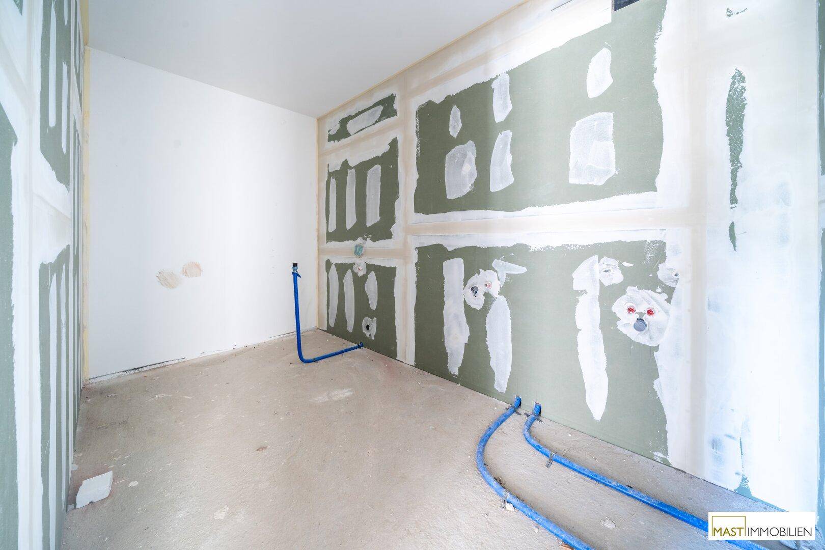 Rohbau eines Badezimmers mit vorbereiteten Anschlüssen für Sanitäranlagen und Trockenbauwänden.