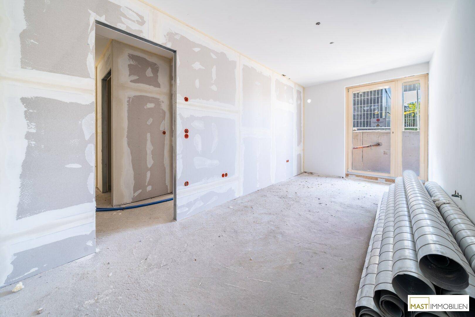 Unfertiger Raum mit Trockenbauwänden, Betonboden und einem Fenster, bereit für den Innenausbau.