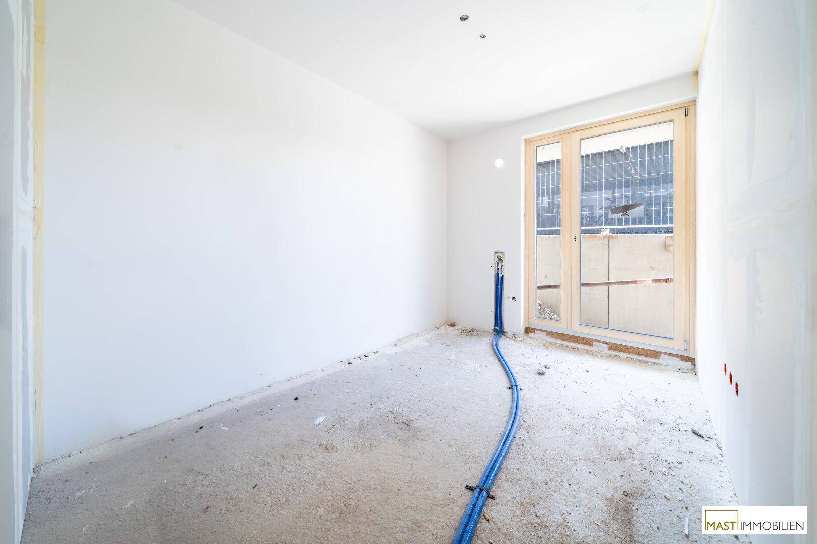 Heller, unfertiger Raum mit großen Fenstern und sichtbaren Installationen auf dem Betonboden.