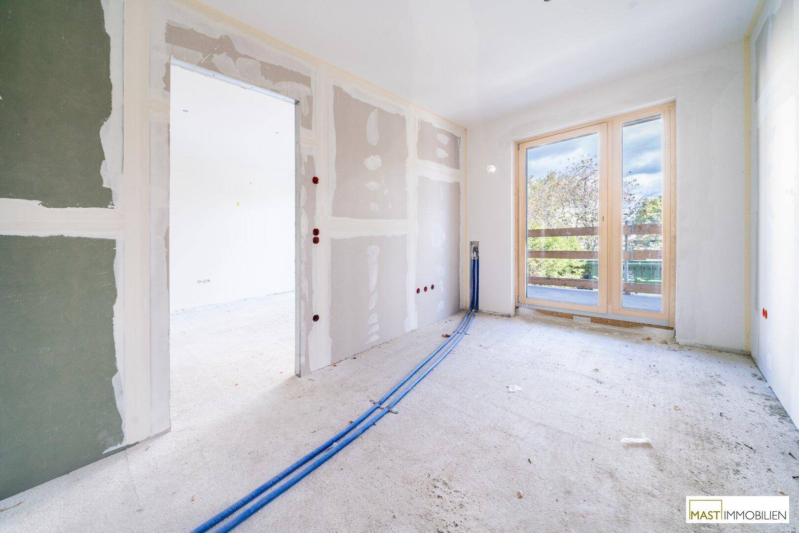 Unfertiger Raum mit Trockenbauwänden, sichtbaren Leitungen und Zugang zu einem potenziellen Balkon.