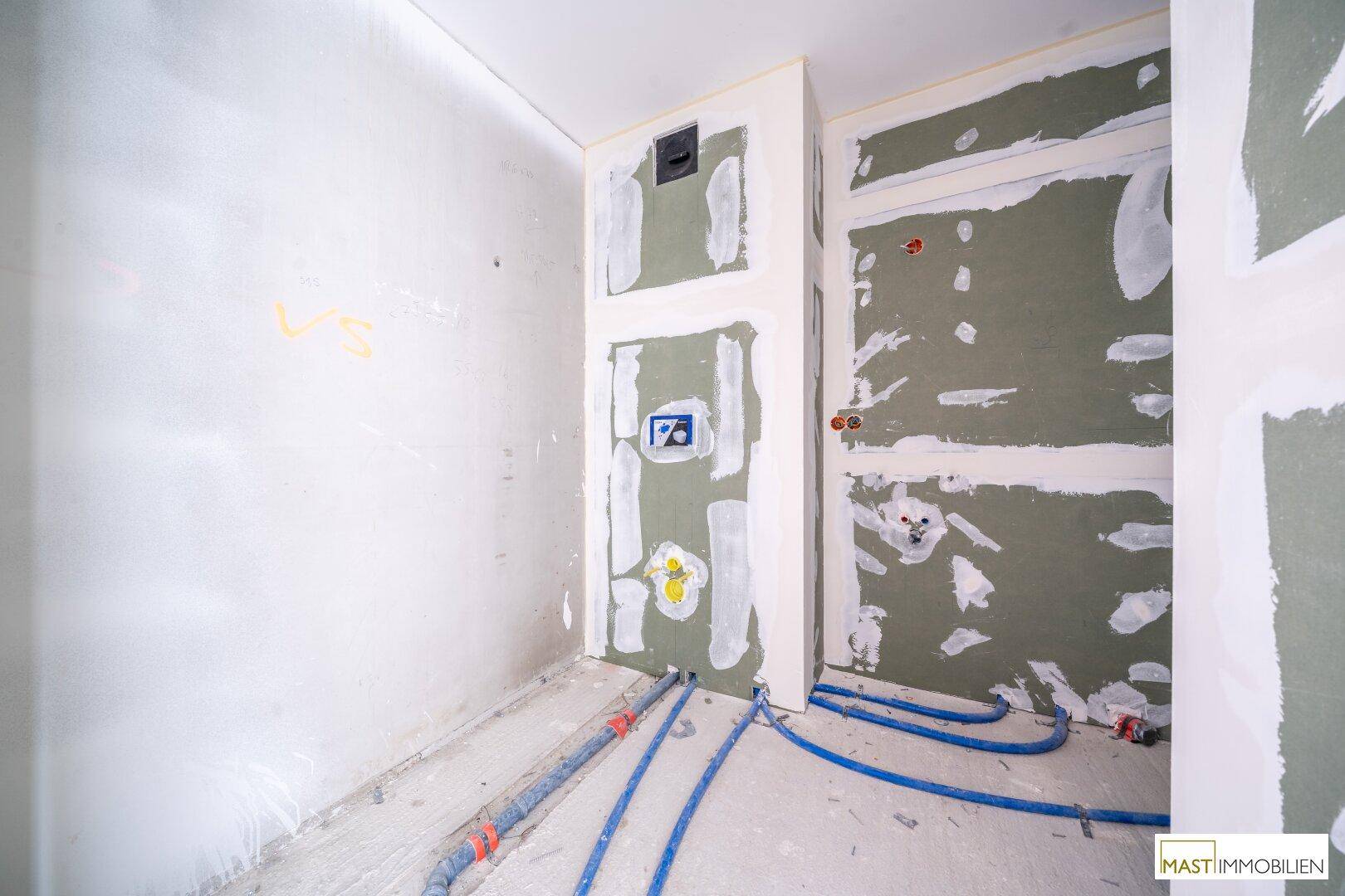Badezimmer im Rohbau mit vorbereiteten Anschlüssen für Sanitärinstallationen und grünen Trockenbauplatten.