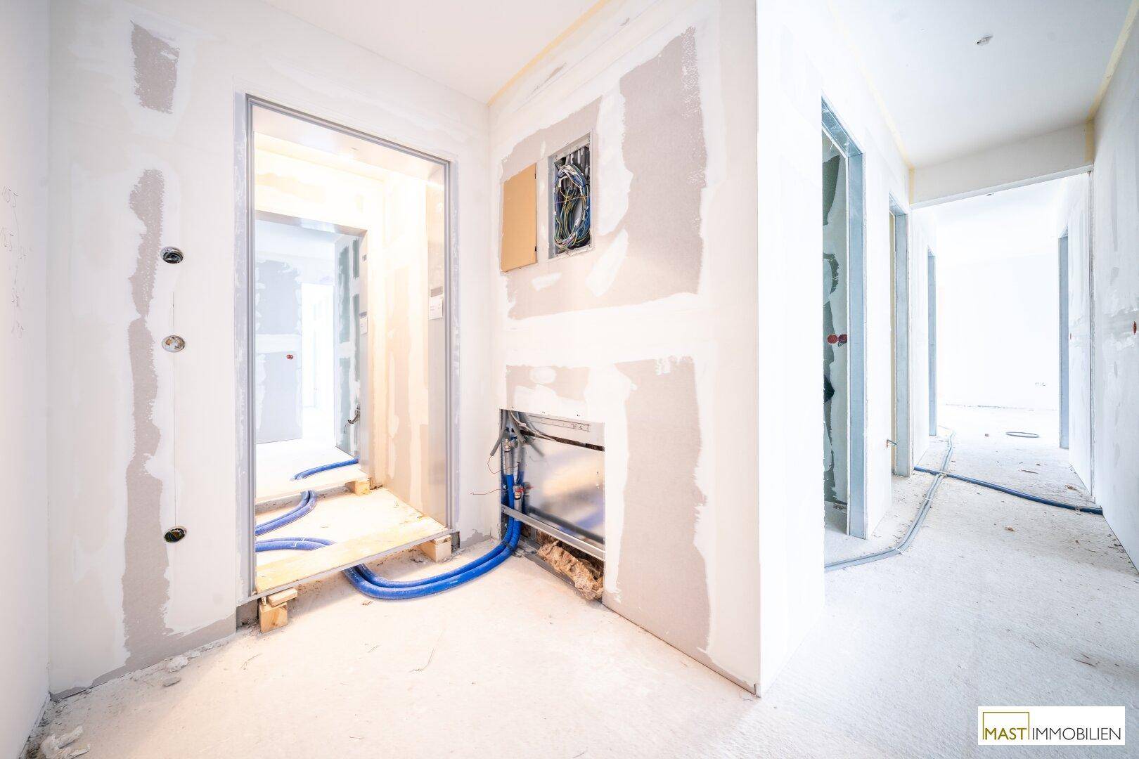 Unfertiger Flurbereich mit sichtbaren Installationen und Türöffnungen, bereit für den Ausbau.
