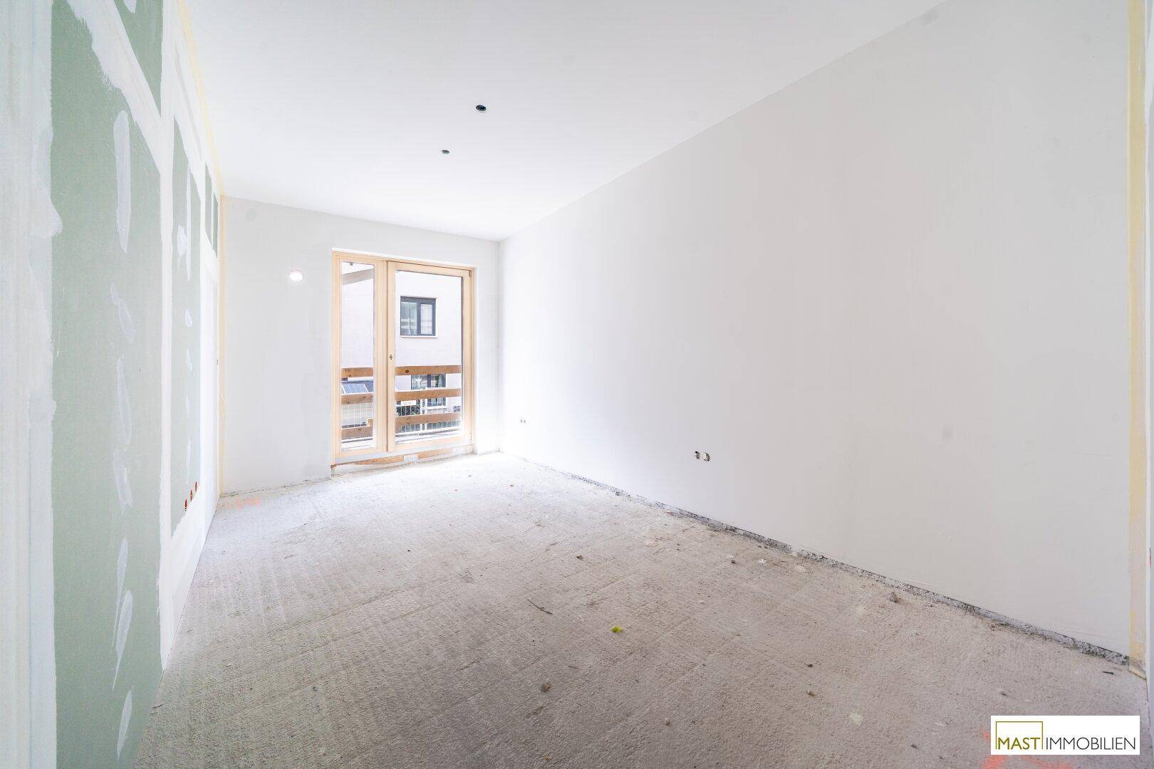 Helles, unfertiges Schlafzimmer mit Betonboden und großem Fenster, bereit für den Innenausbau.
